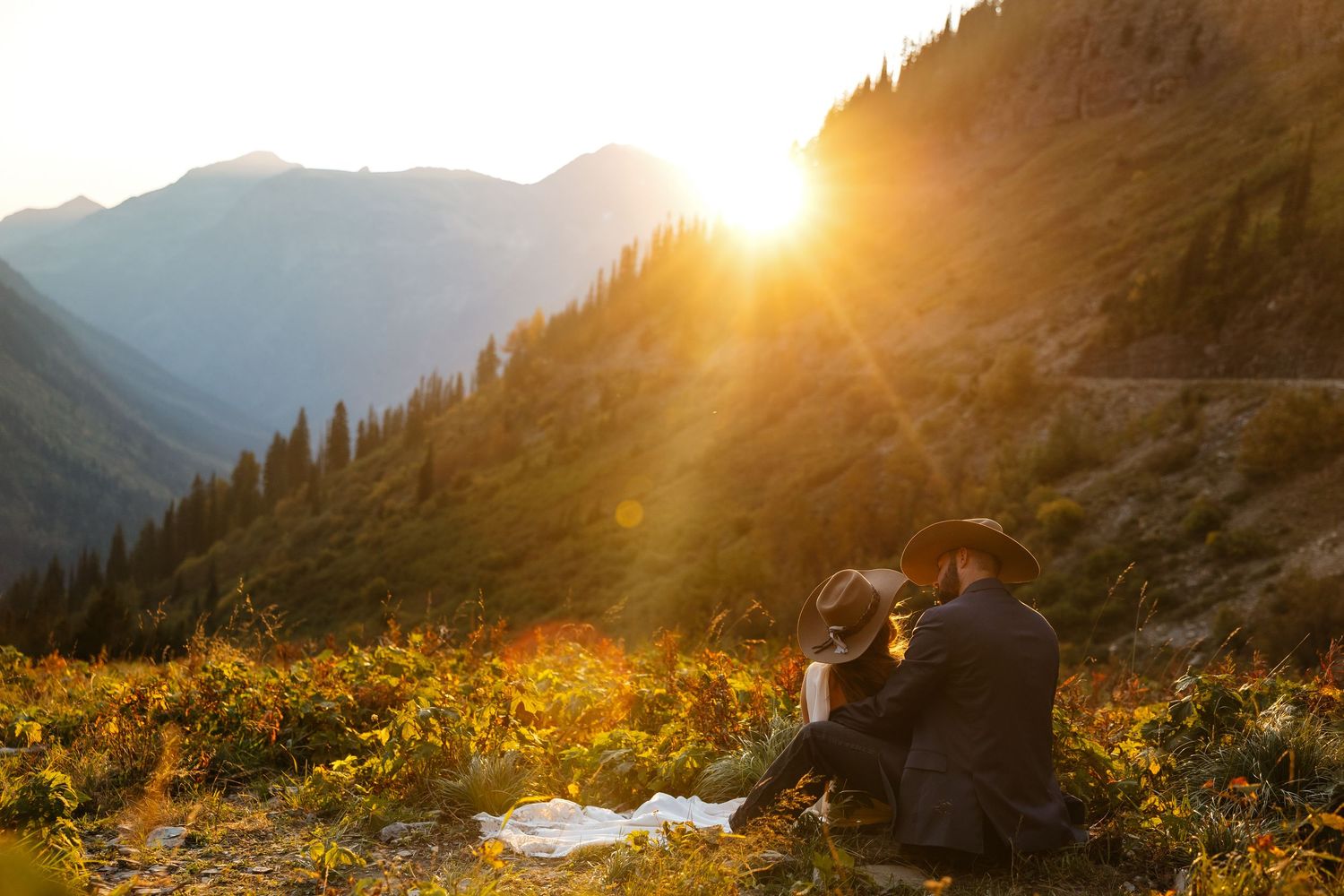 Golden sunlight breaks through mountain peaks casting warm rays across a scenic alpine landscape at sunset.