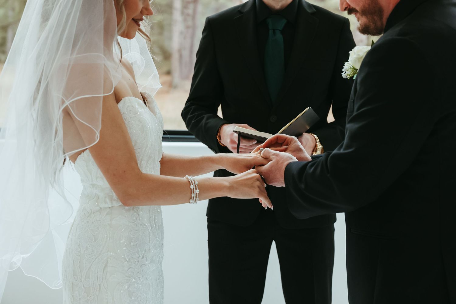 A close-up shot of a wedding ceremony showing hands exchanging rings with an officiant holding paperwork.