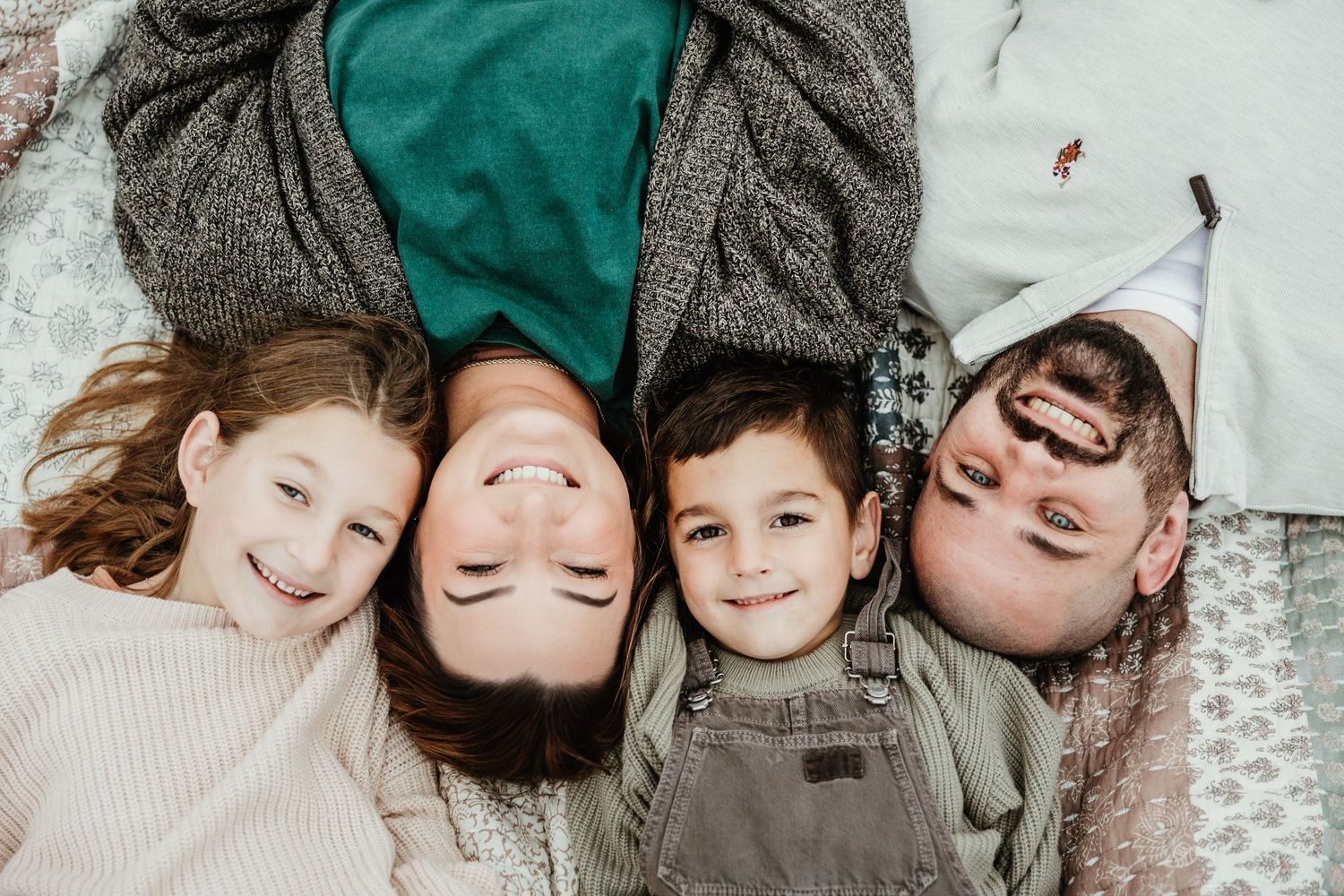 Four people lying down on a blanket together smiling while looking upwards during a joyful outdoor moment.