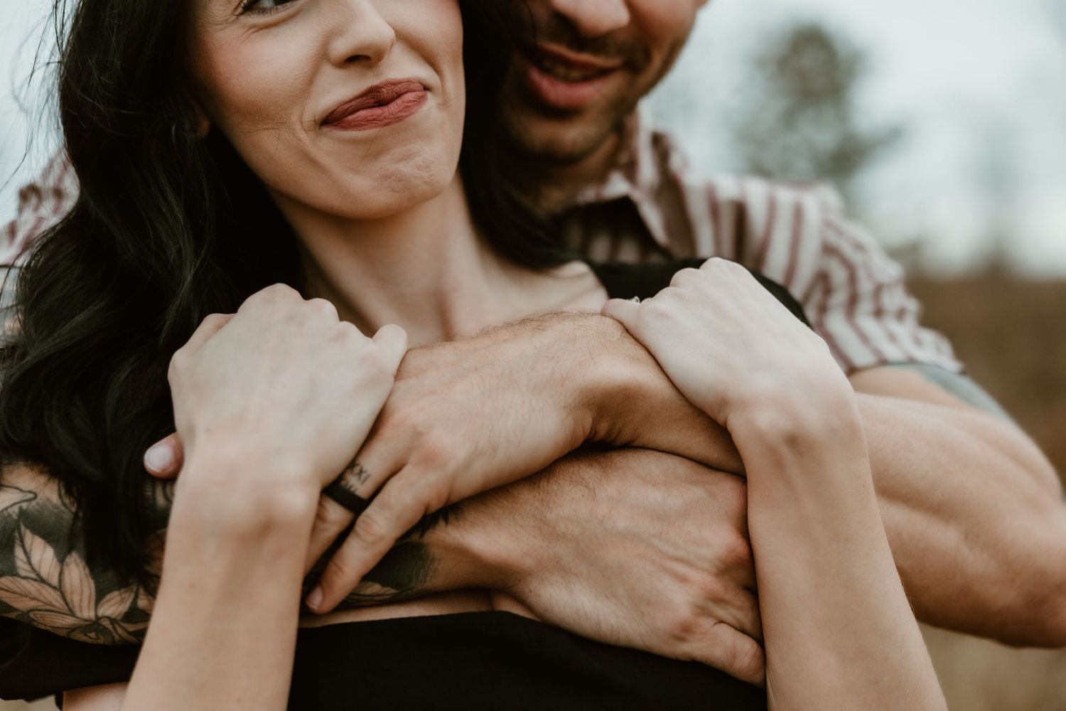 A close up of a couple embracing and smiling together outdoors.