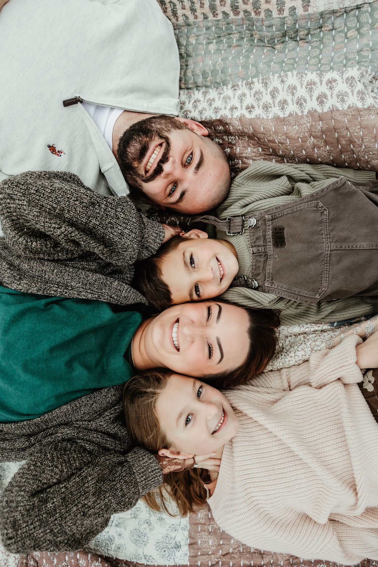 Overhead view of four people laying in a circle with their heads together on a textured blanket.