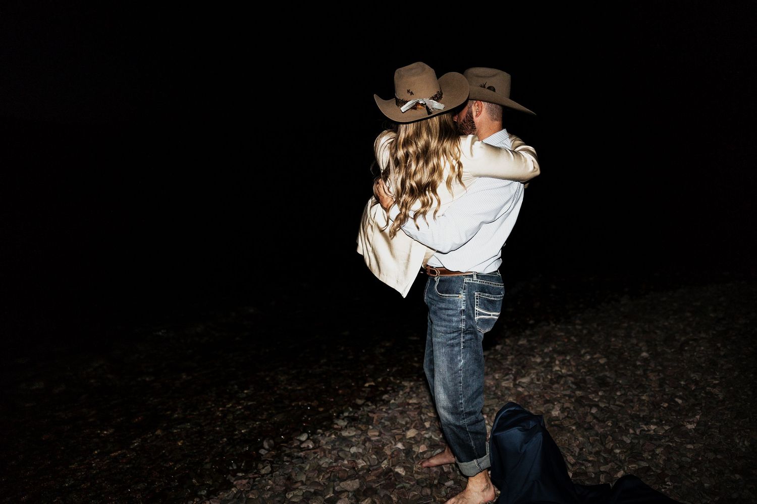 A couple embraces in western wear against a dark background.