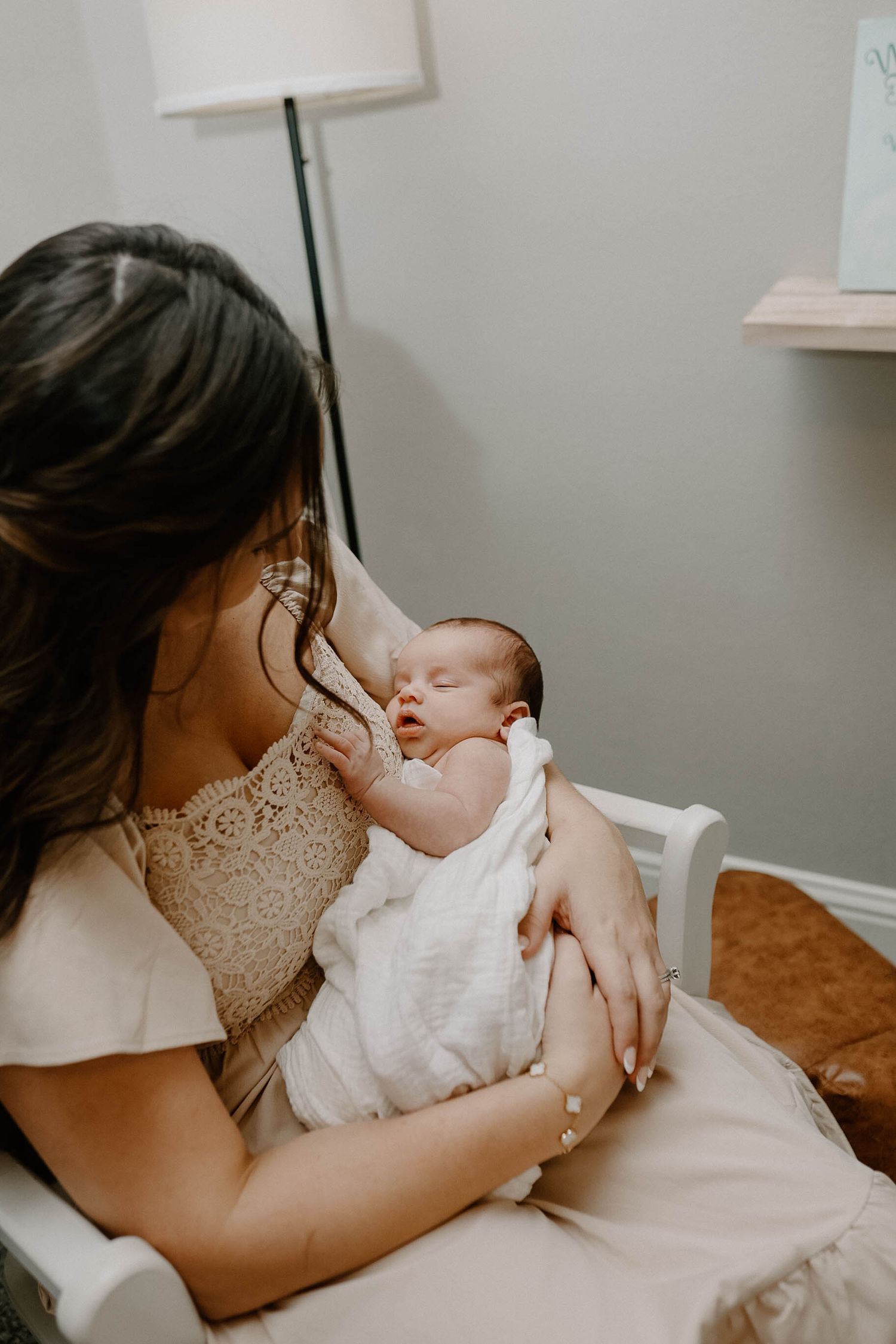 A sleeping newborn baby wearing white clothes rests peacefully in their mother's arms in a nursery setting.