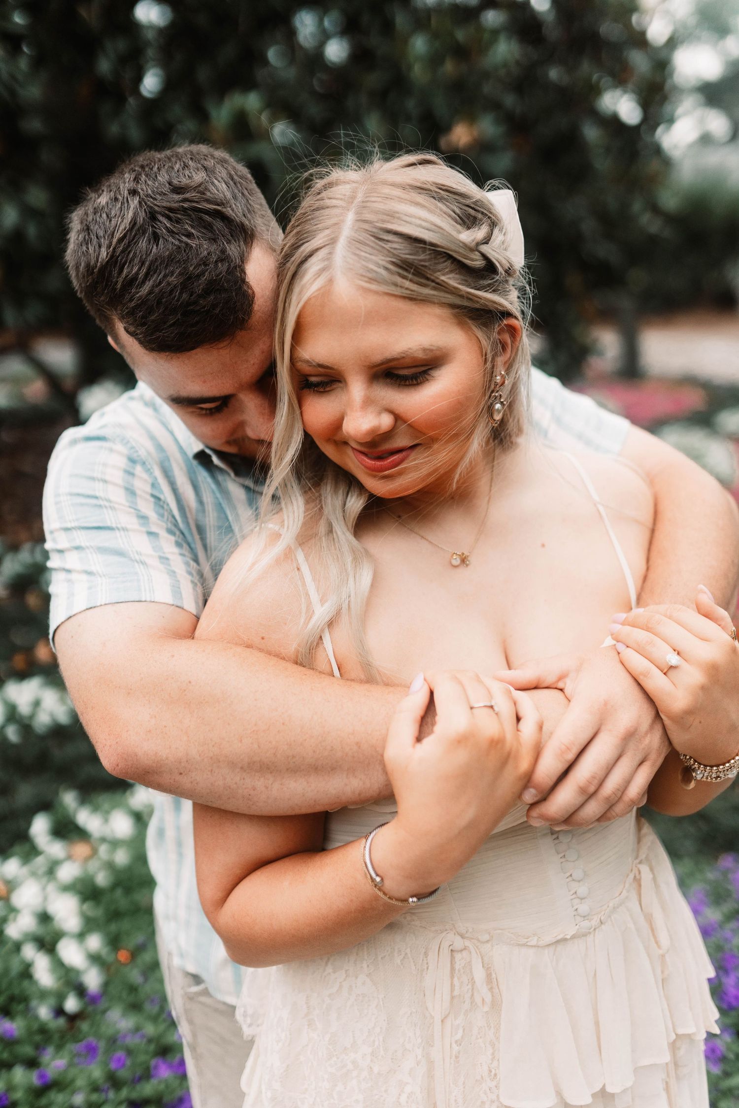 A romantic embrace captured in a garden setting with soft lighting and greenery in the background.