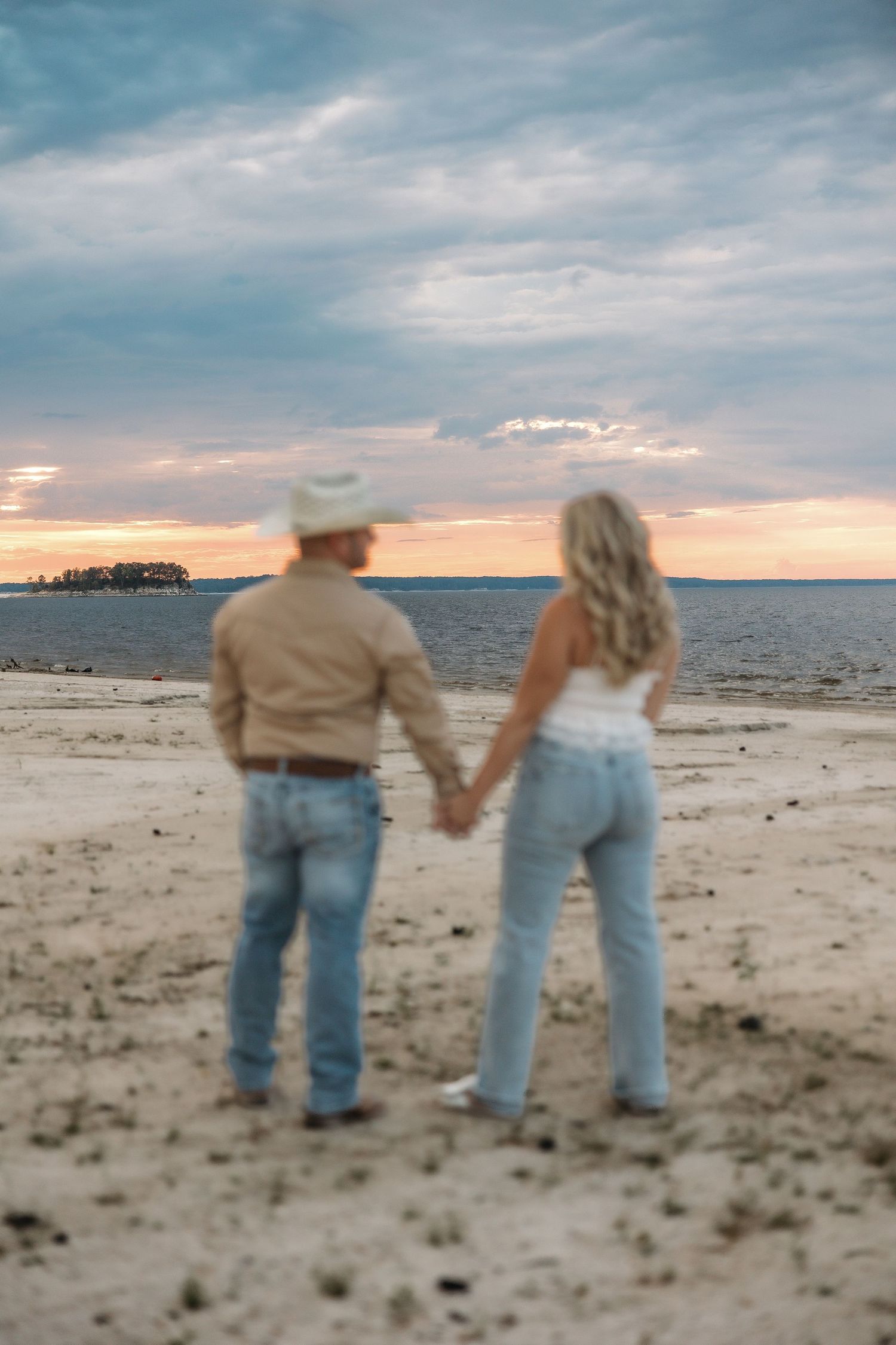 Silhouettes of a couple walking along a beach shoreline at dusk with cloudy skies overhead.
