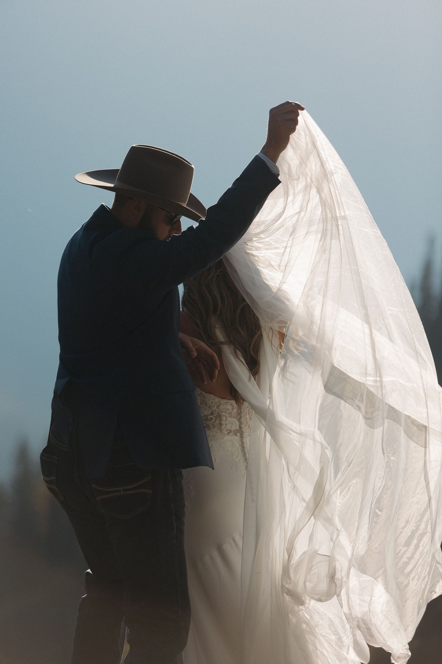 A couple embraces outdoors with one person wearing a flowing white dress and the other in dark attire.
