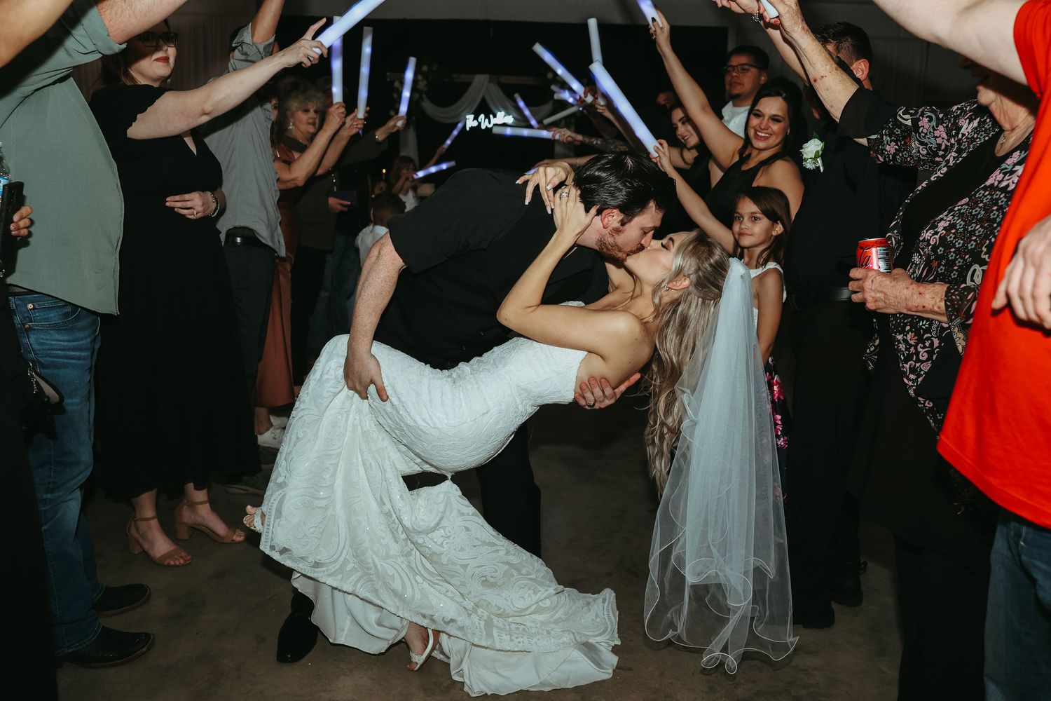 Wedding guests form a tunnel while a bride in a white gown dips during a dance at the reception.