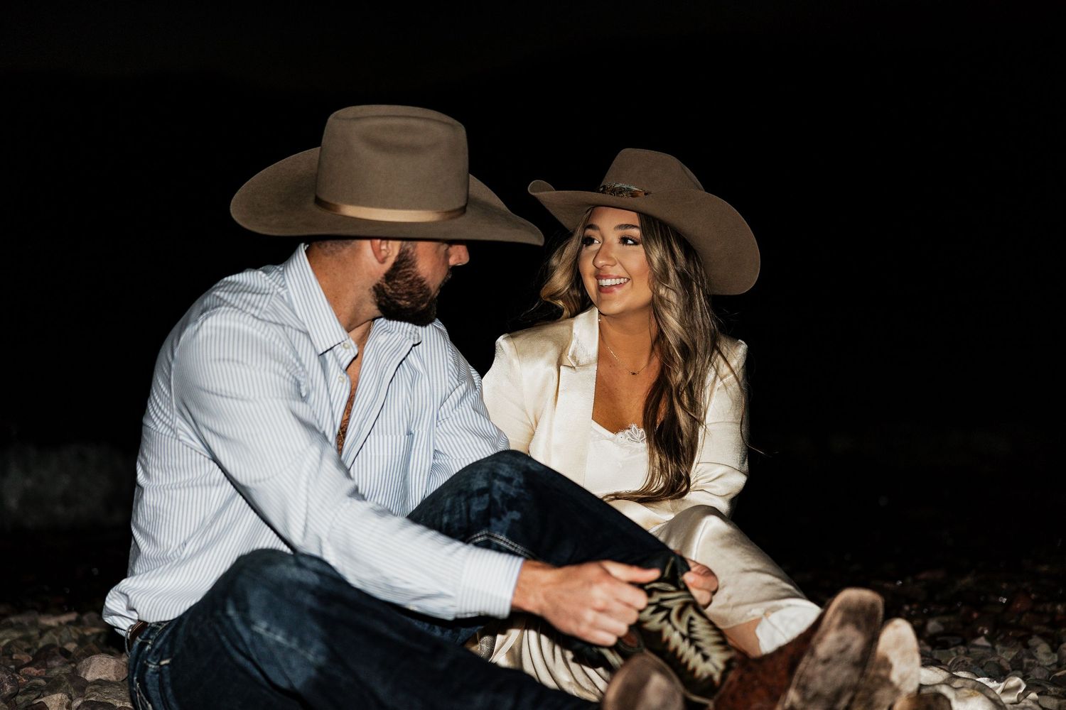 A couple in western attire sharing an intimate moment against a dark background.