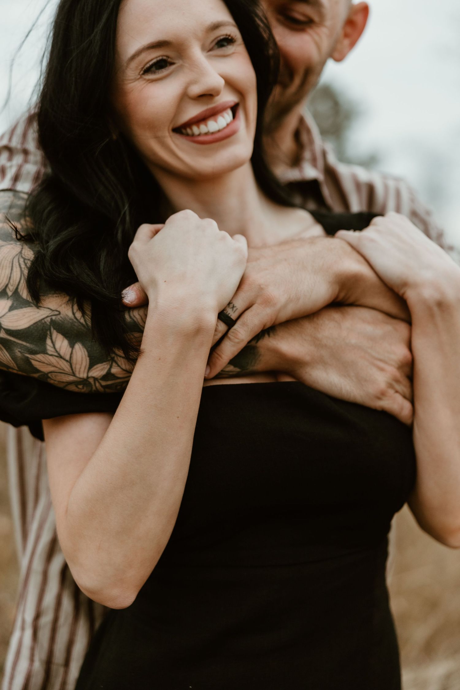 A couple embraces in a candid moment wearing black and neutral colors against a light background.