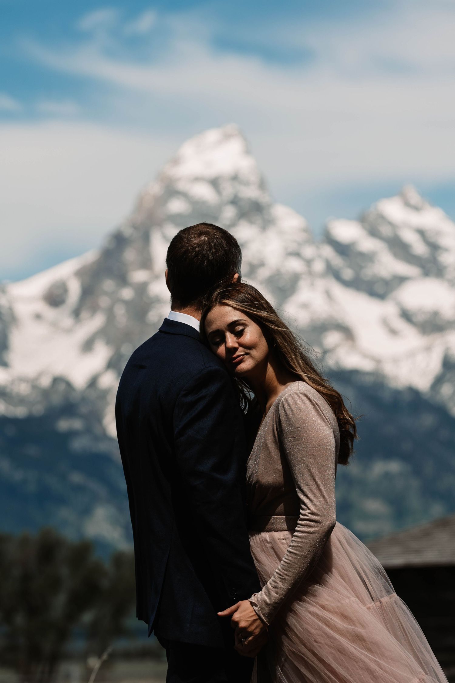 A romantic couple embraces against the backdrop of snow-capped Grand Teton mountains in Wyoming.