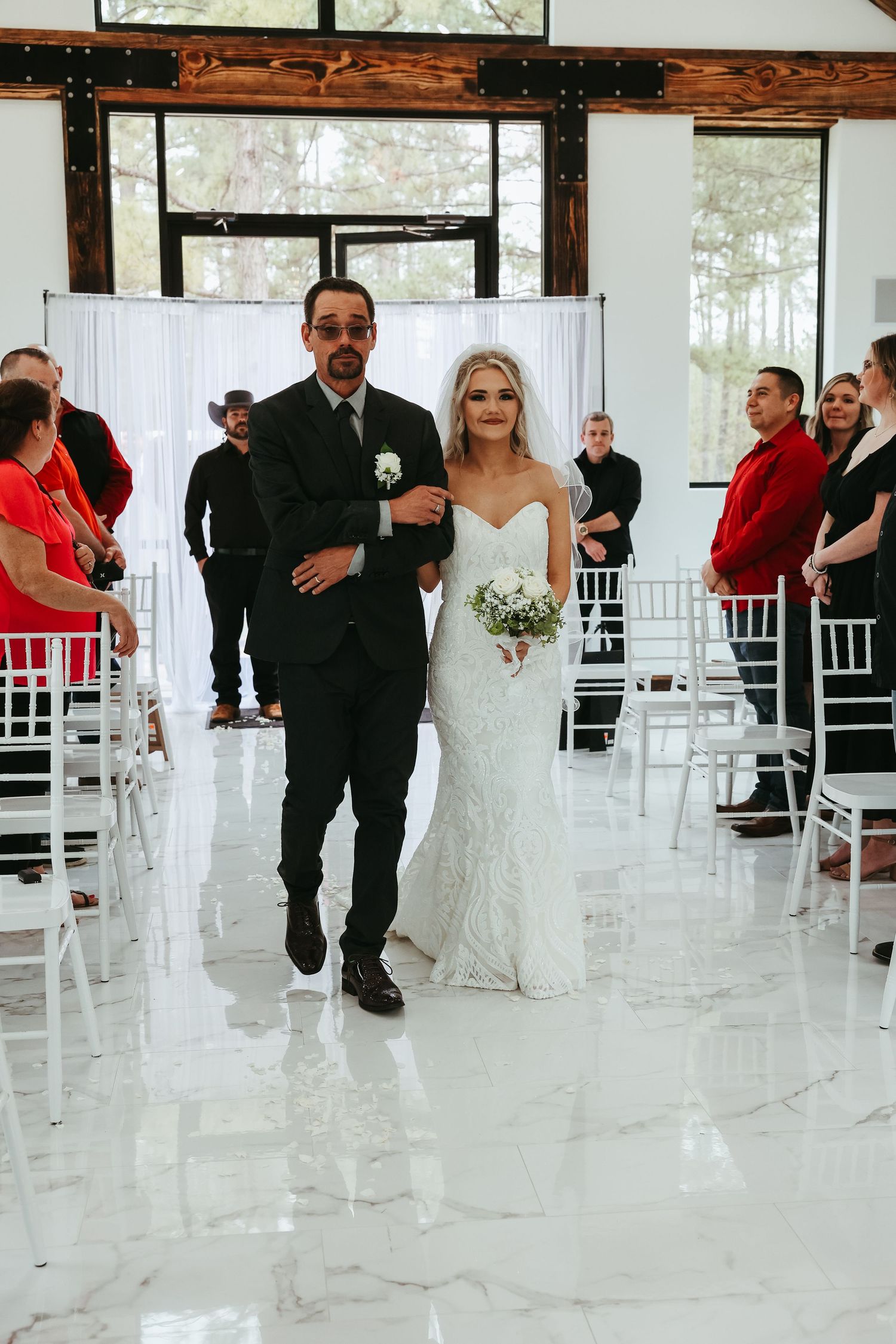 A wedding procession moment showing a bride in a fitted lace gown walking down the aisle at an elegant indoor venue.