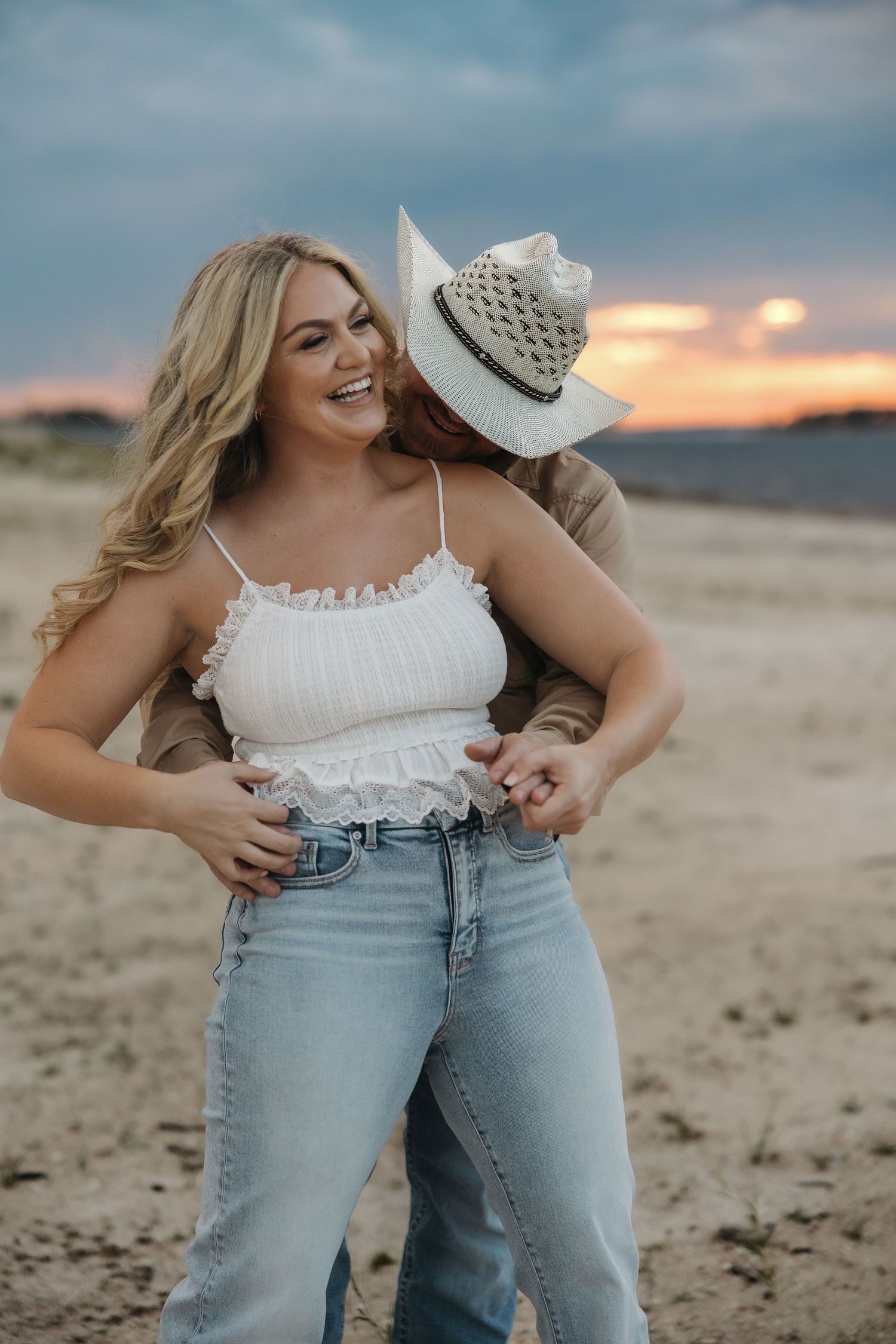 A couple shares a candid moment at sunset in a desert setting wearing western-inspired outfits.