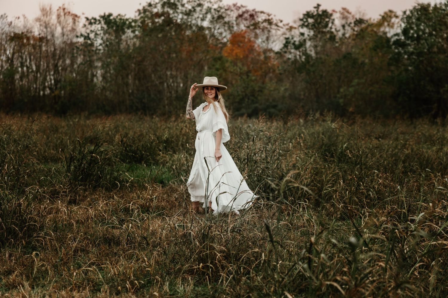 A flowing white dress stands out against an autumn field as golden light illuminates the natural landscape.
