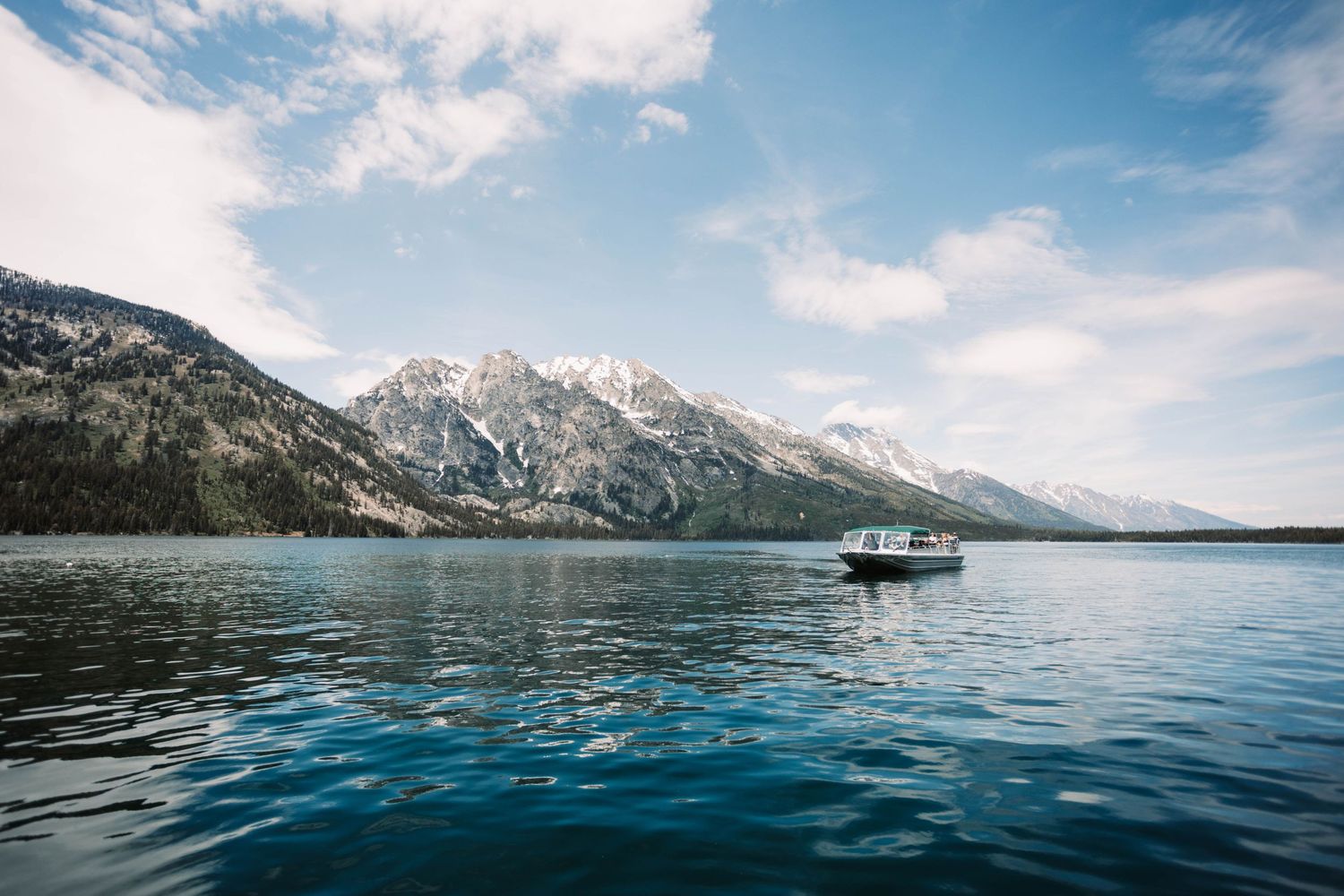 Small boat cruises across turquoise Jenny Lake with snow-capped Teton Mountains rising majestically in Grand Teton National Park.