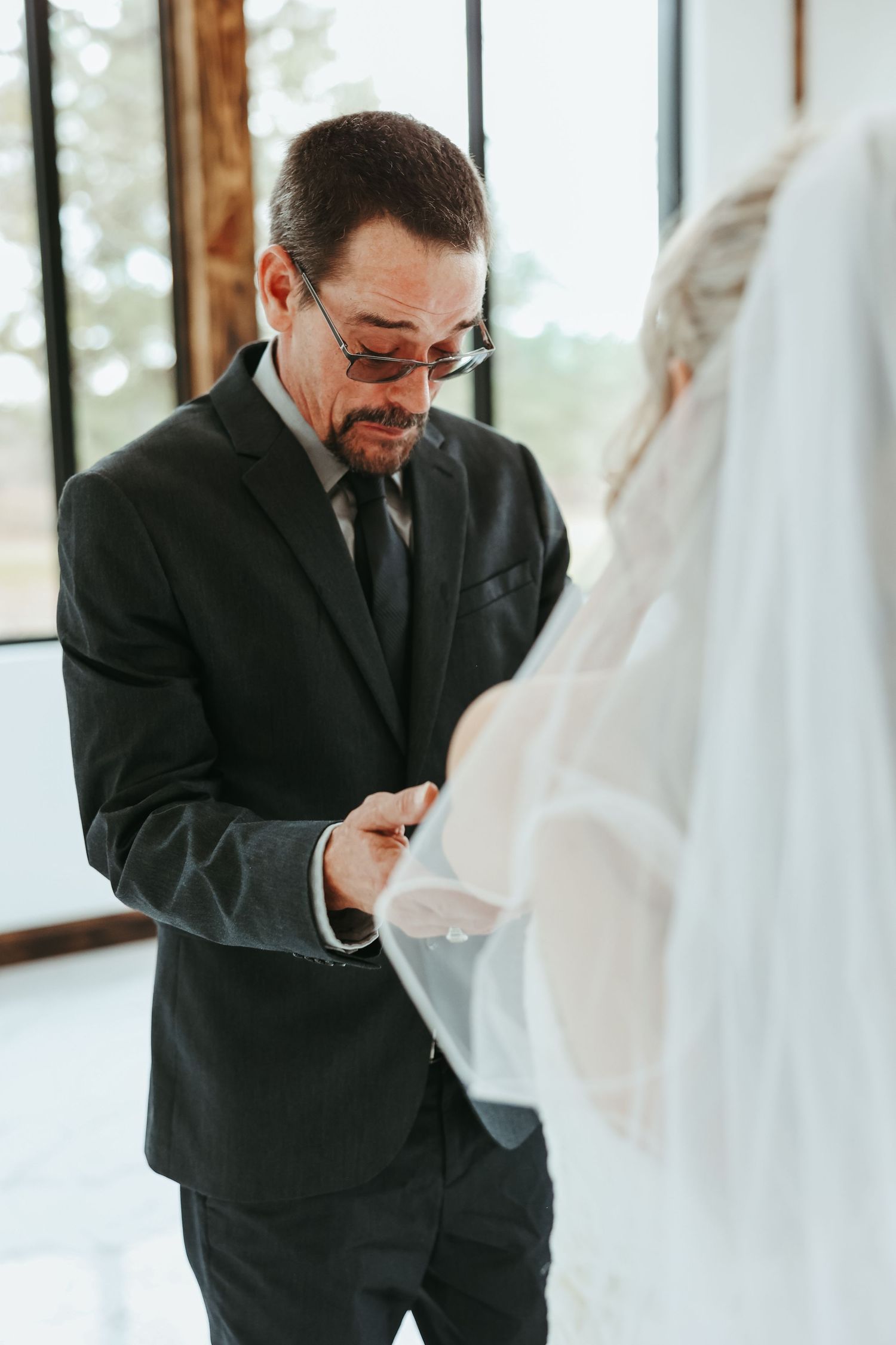 An emotional moment captured during a wedding ceremony as a guest in a black suit and glasses reacts with joy.