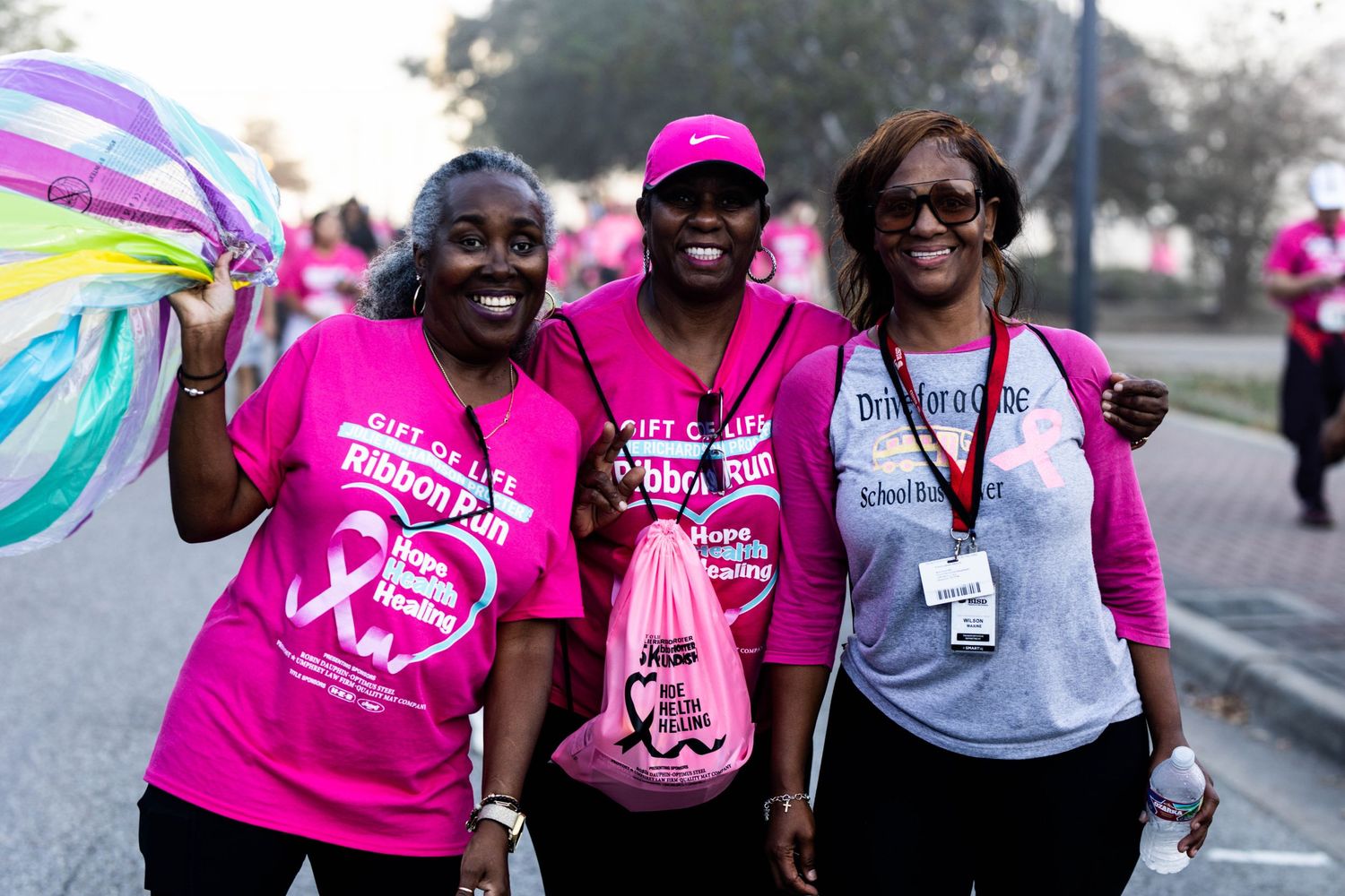 Group of supporters wearing bright pink shirts participate in breast cancer awareness walk event.
