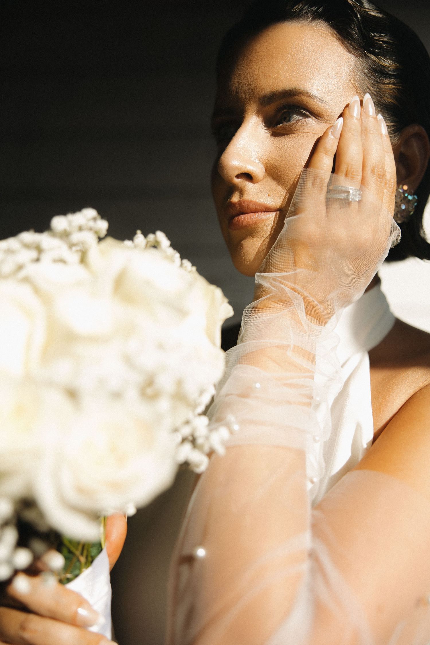 Close-up artistic bridal portrait with soft lighting and white roses creating a dreamy atmosphere.