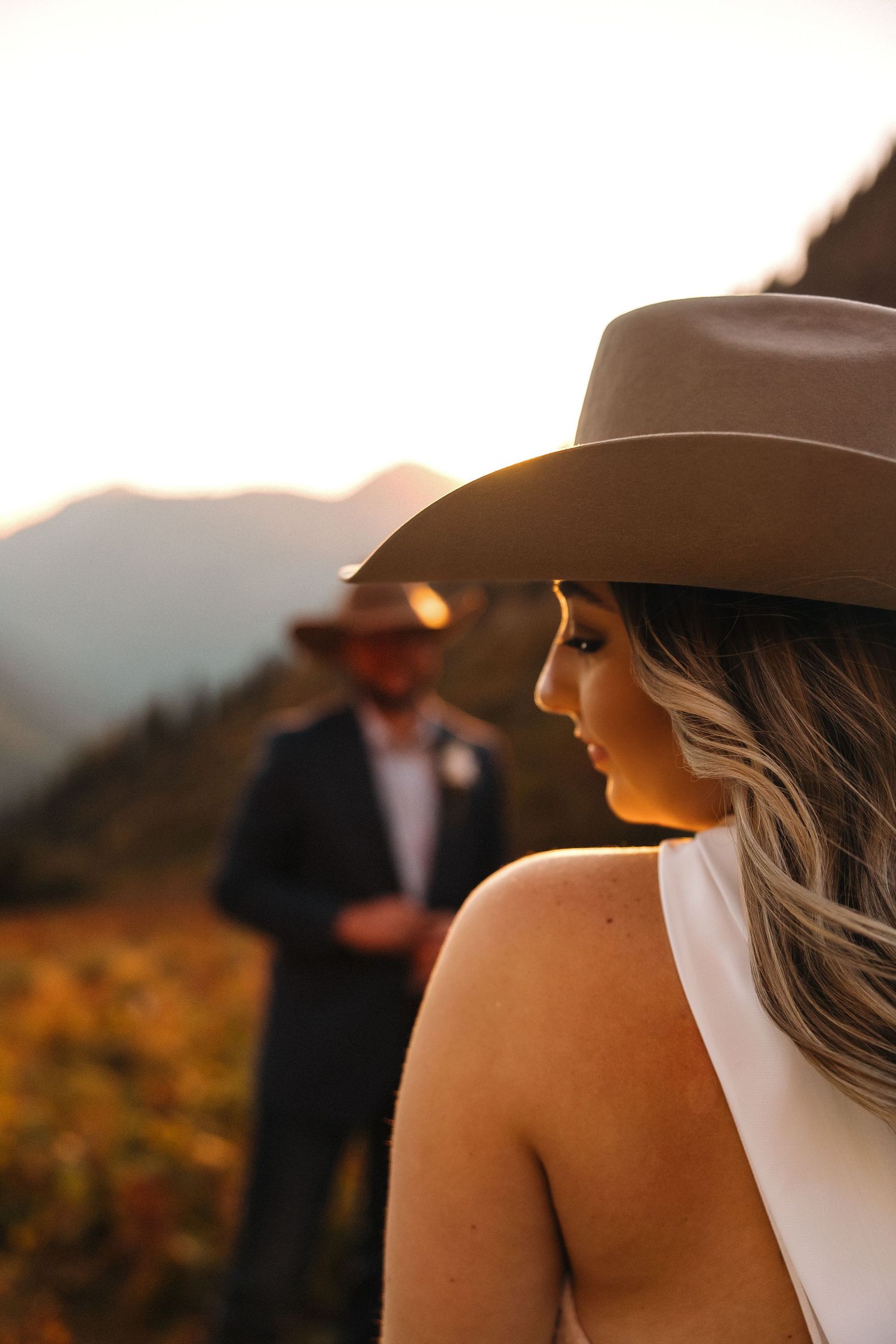 Cowboy hats silhouetted against a warm sunset in a mountainous landscape.