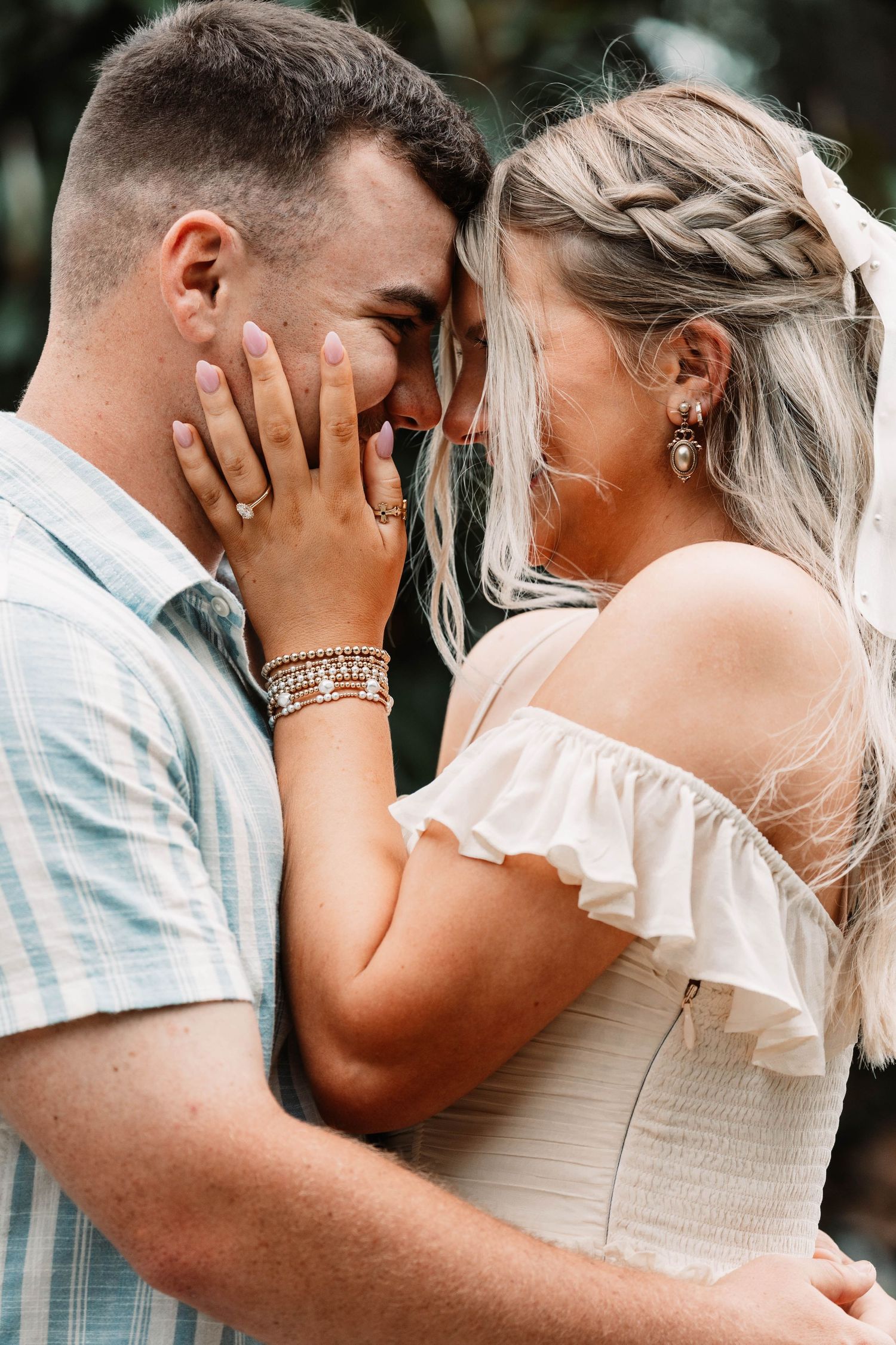 A romantic moment captured showing an intimate embrace, with braided blonde hair and off-shoulder dress details.