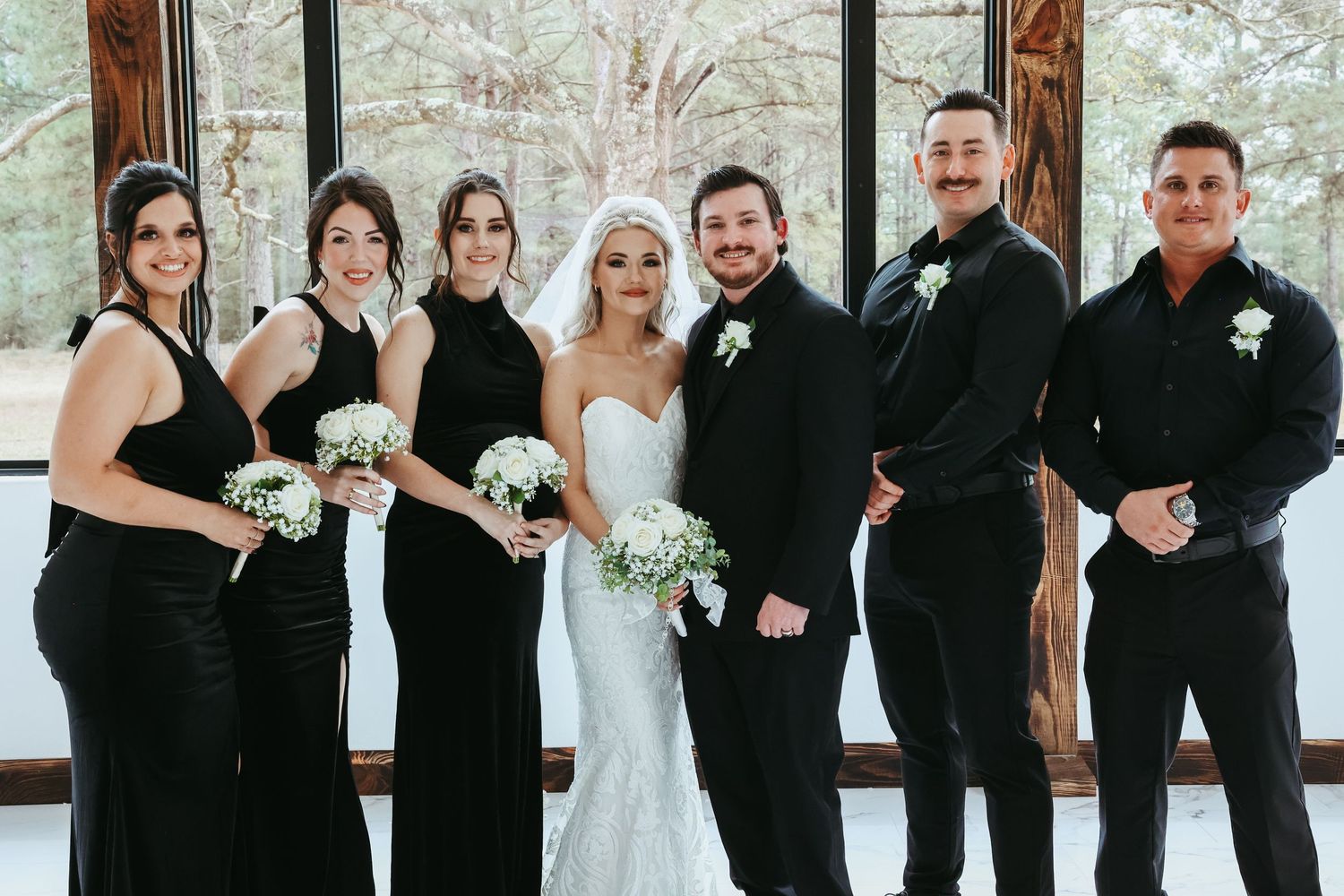 A wedding party poses together in formal black attire with a bride in a traditional white wedding gown.