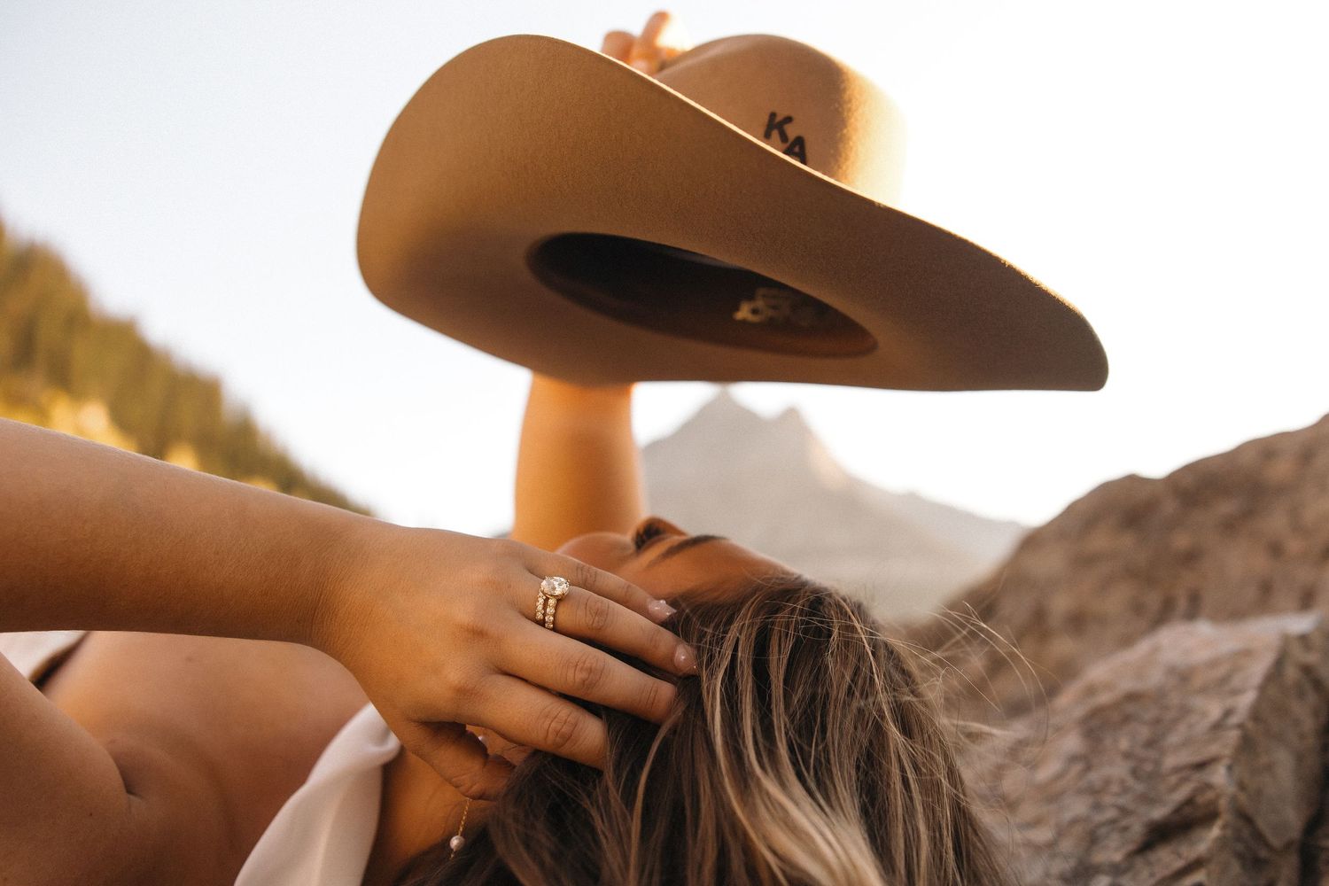 Two people embrace in a romantic moment against a stunning mountain backdrop at sunset.