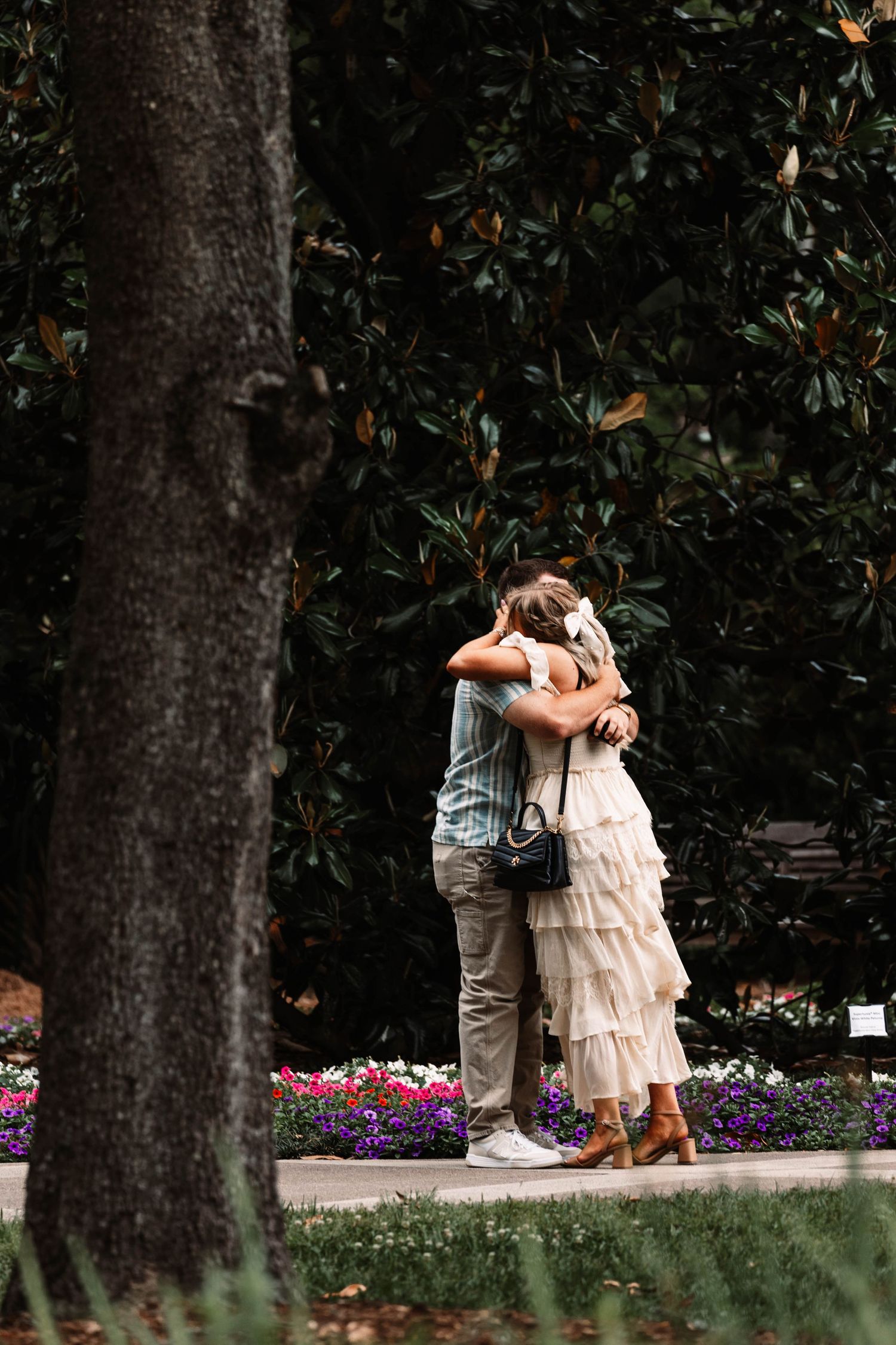 A couple embraces tenderly on a garden path surrounded by colorful flowers and lush greenery in a romantic moment.