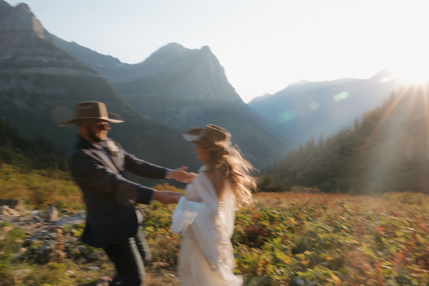 A romantic scene unfolds as two people stand together among wildflowers with mountains in the distance.