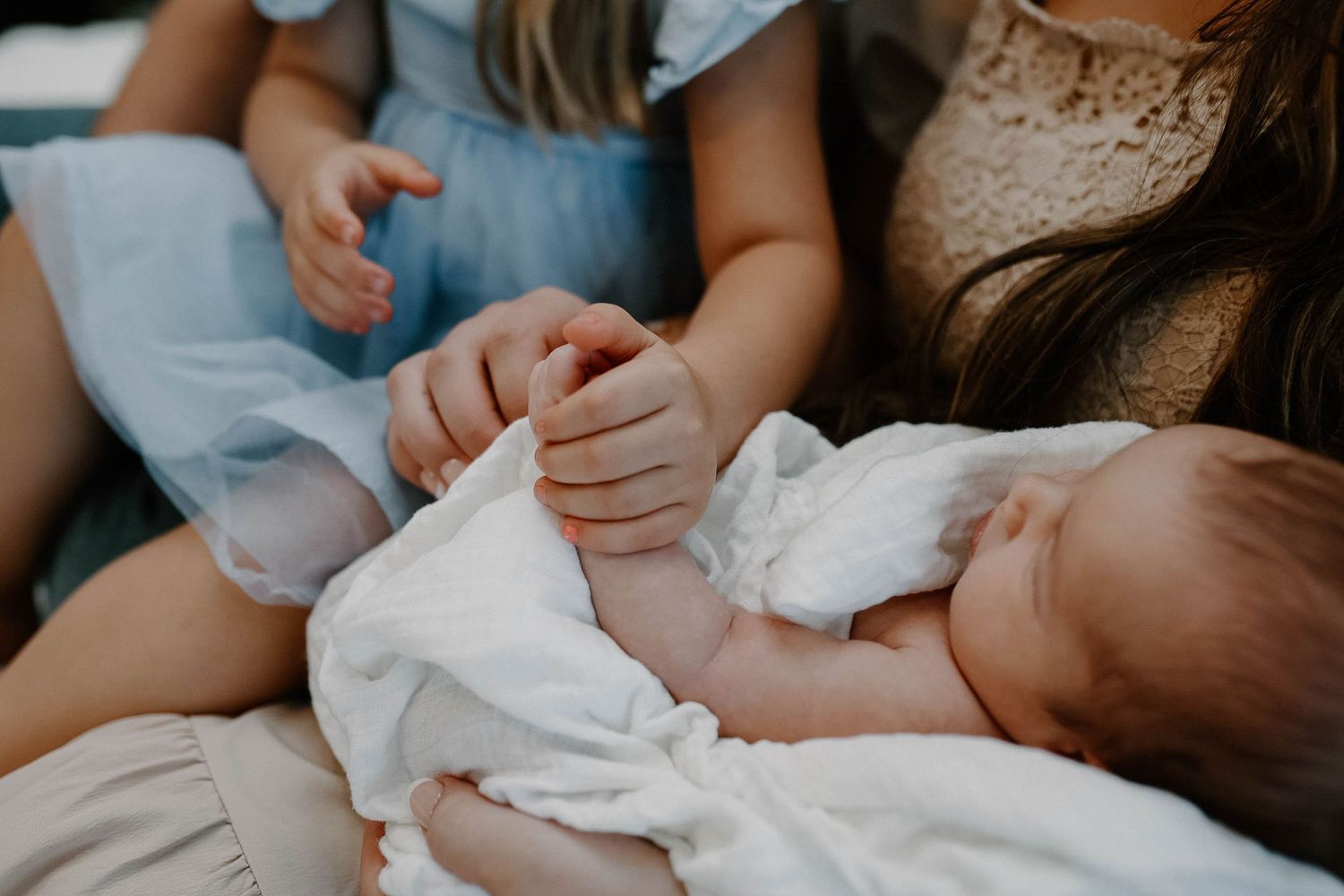 A tender moment captured as caring hands gently hold a sleeping baby swaddled in white fabric.