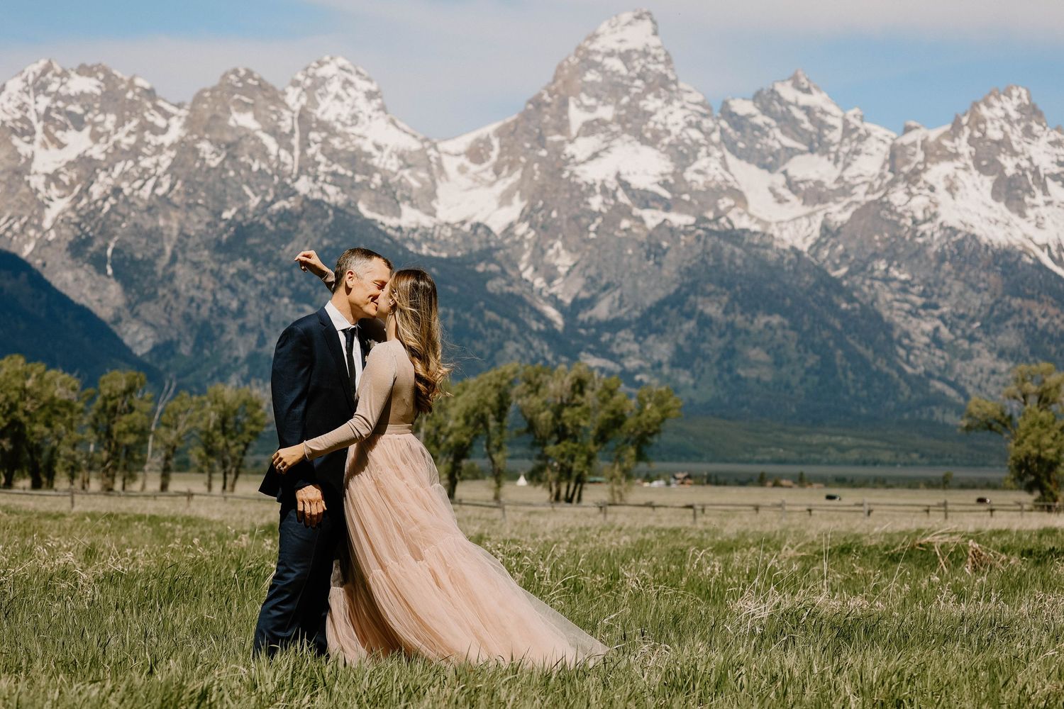 A couple embraces in a meadow with the majestic Grand Teton mountains rising dramatically in the background.