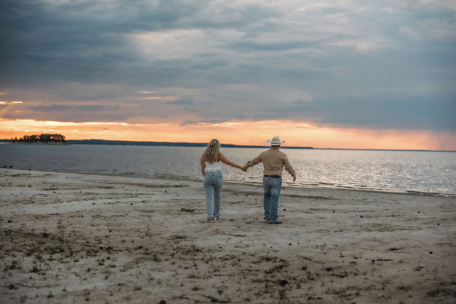 Two people strolling together on a sandy beach during golden hour with moody clouds above.