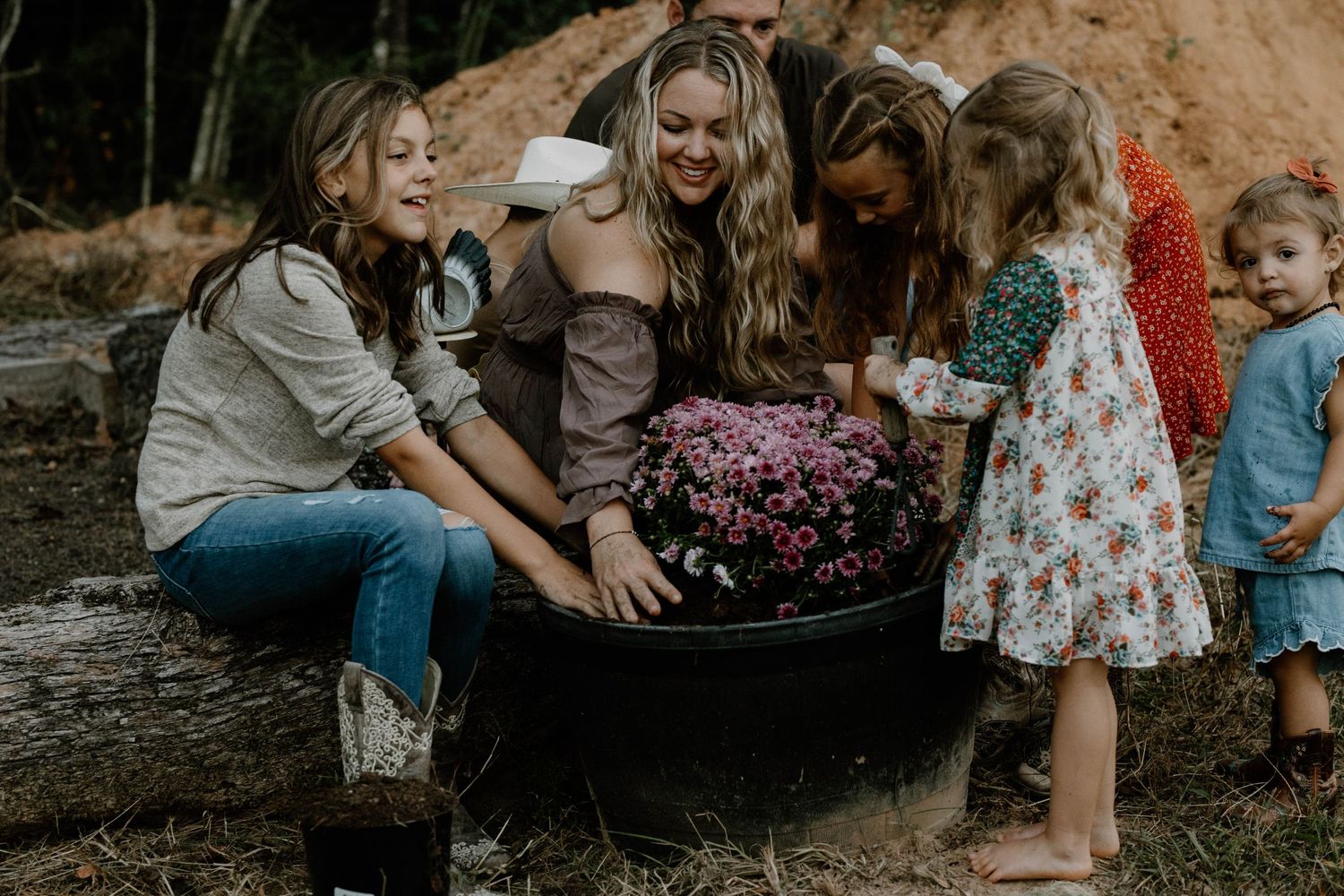 Group gathered around a large planter filled with pink mums in an outdoor garden setting.