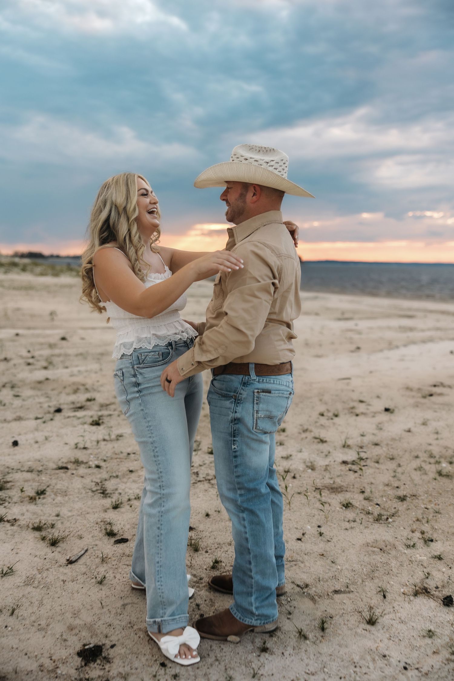 Two people share an intimate dance moment on sandy terrain during golden hour.