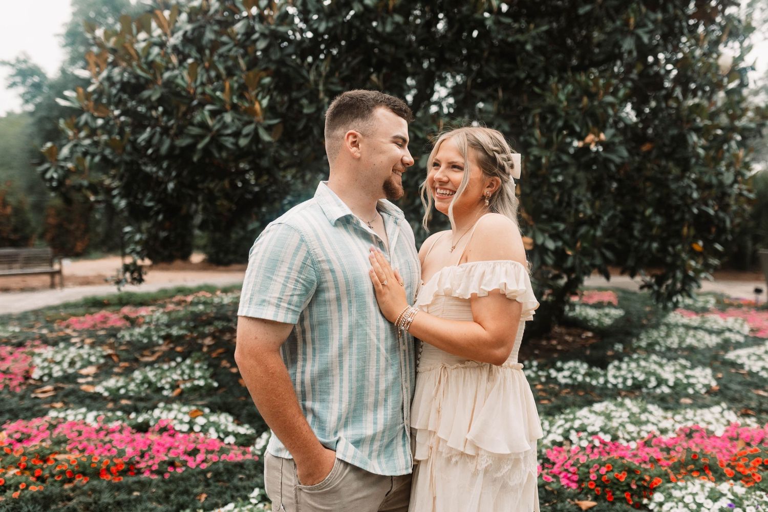 A couple shares a joyful moment together in a garden with blooming pink flowers and magnolia trees.