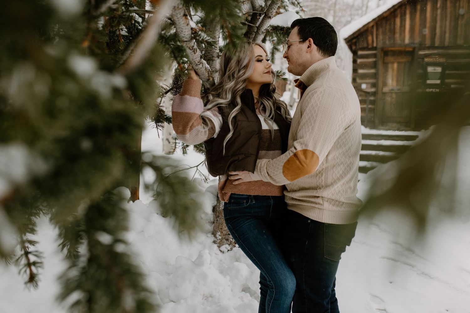 A romantic winter scene with a couple embracing in front of a rustic cabin in the snow.