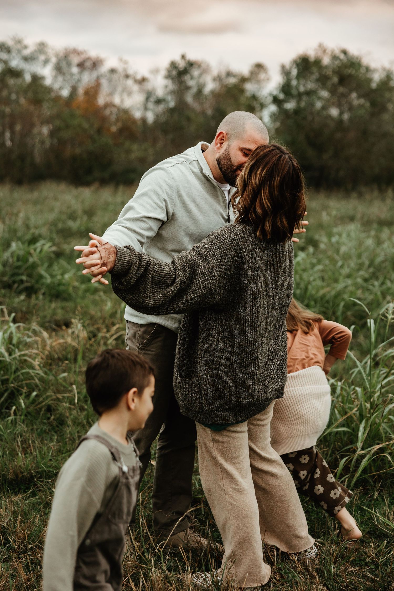 A family shares an intimate moment while dancing together in a rustic field during golden hour.