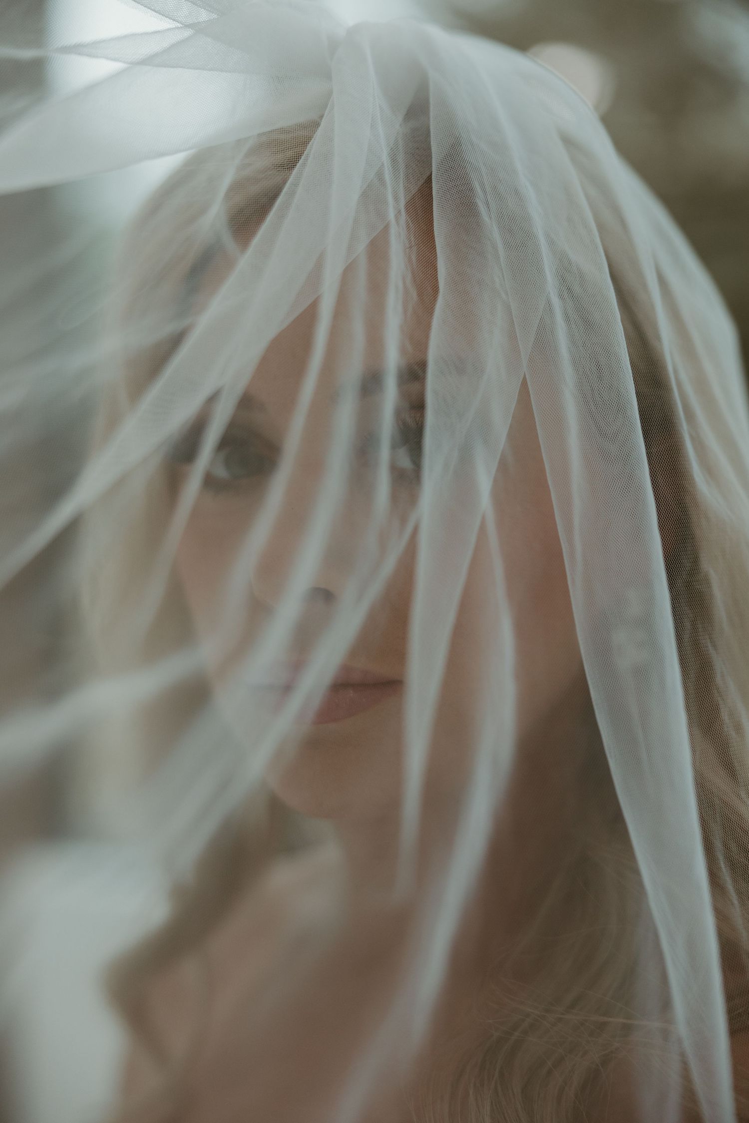A delicate white bridal veil creates a soft, ethereal effect in an artistic close-up portrait photograph.