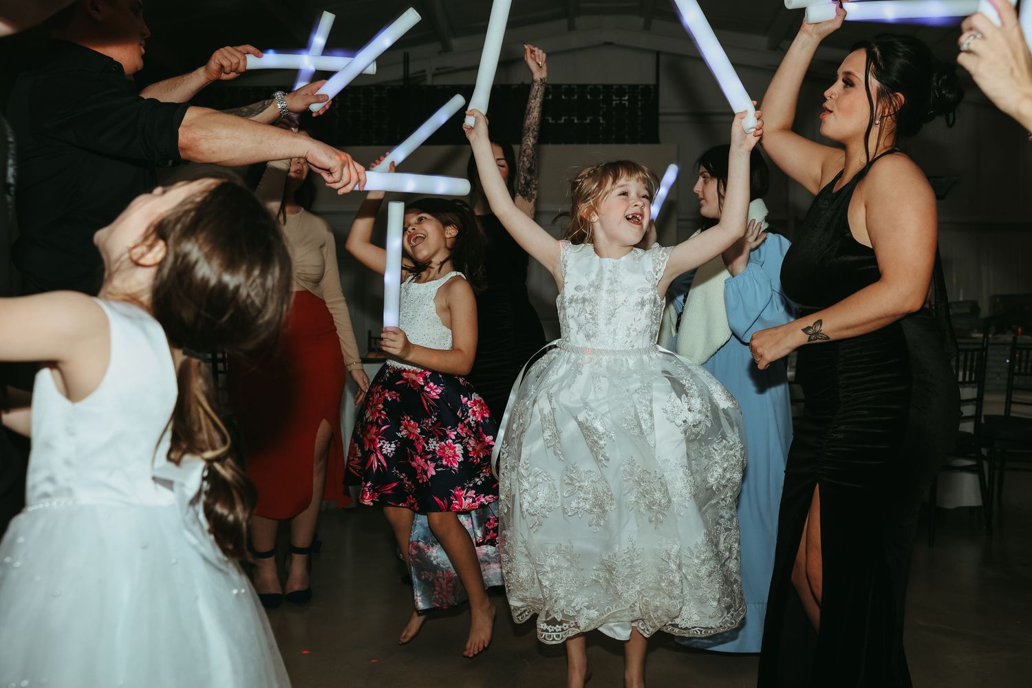 People dancing and celebrating at a wedding reception with glowing blue light sticks on a dark dance floor.