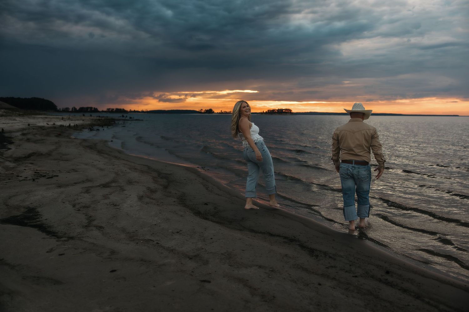 Silhouettes walking along the shoreline against a dramatic orange and blue sunset sky.