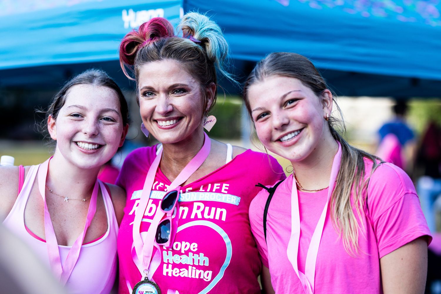 Three participants in pink shirts smile together at breast cancer awareness run.