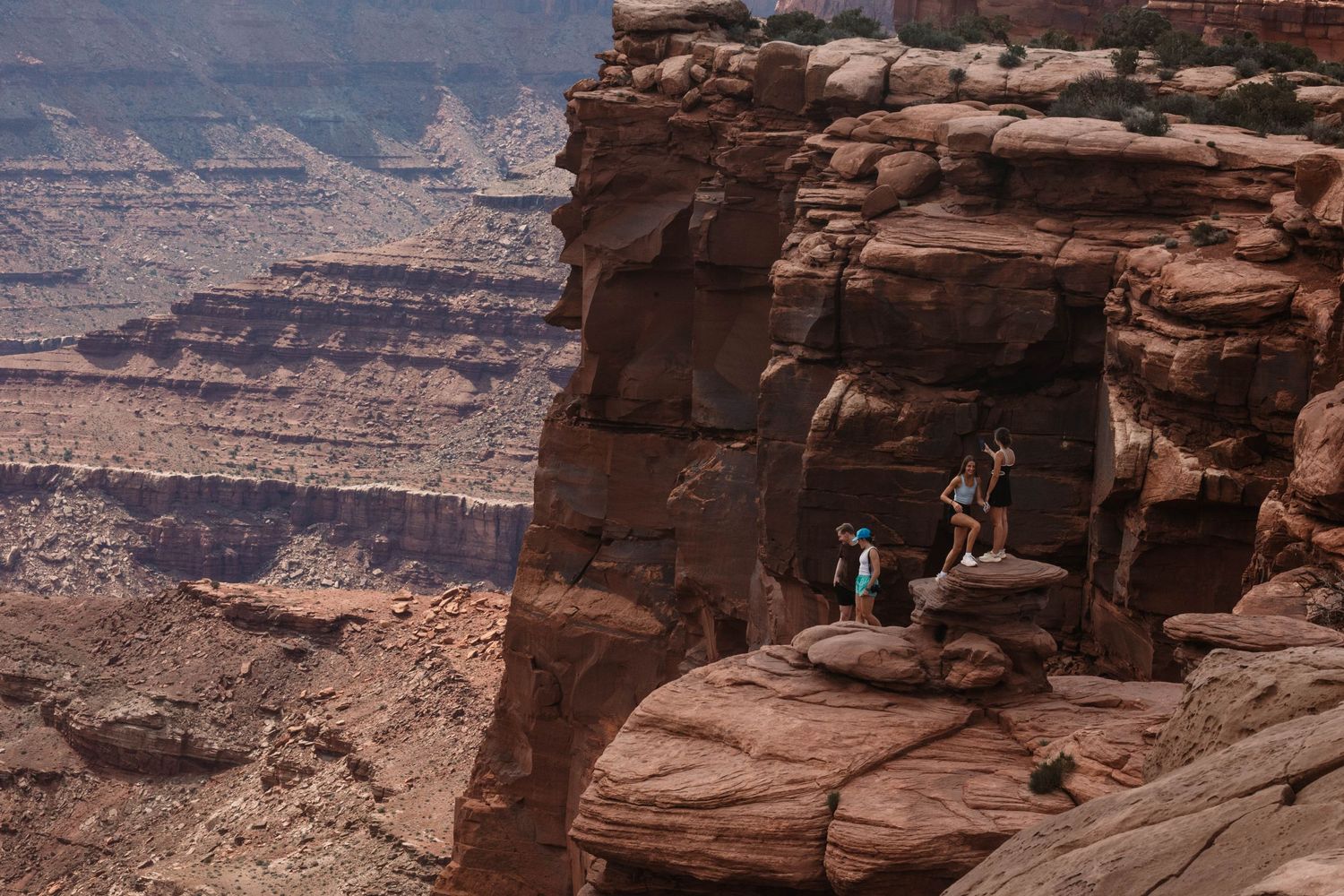 Hikers stand on a dramatic red rock cliff overlooking the vast desert canyons in Canyonlands National Park.