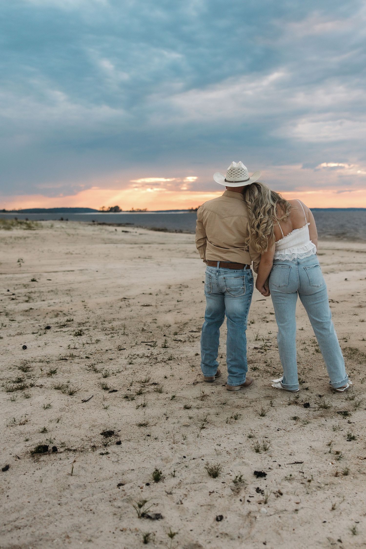 A couple embraces while watching the sunset over a desert landscape.