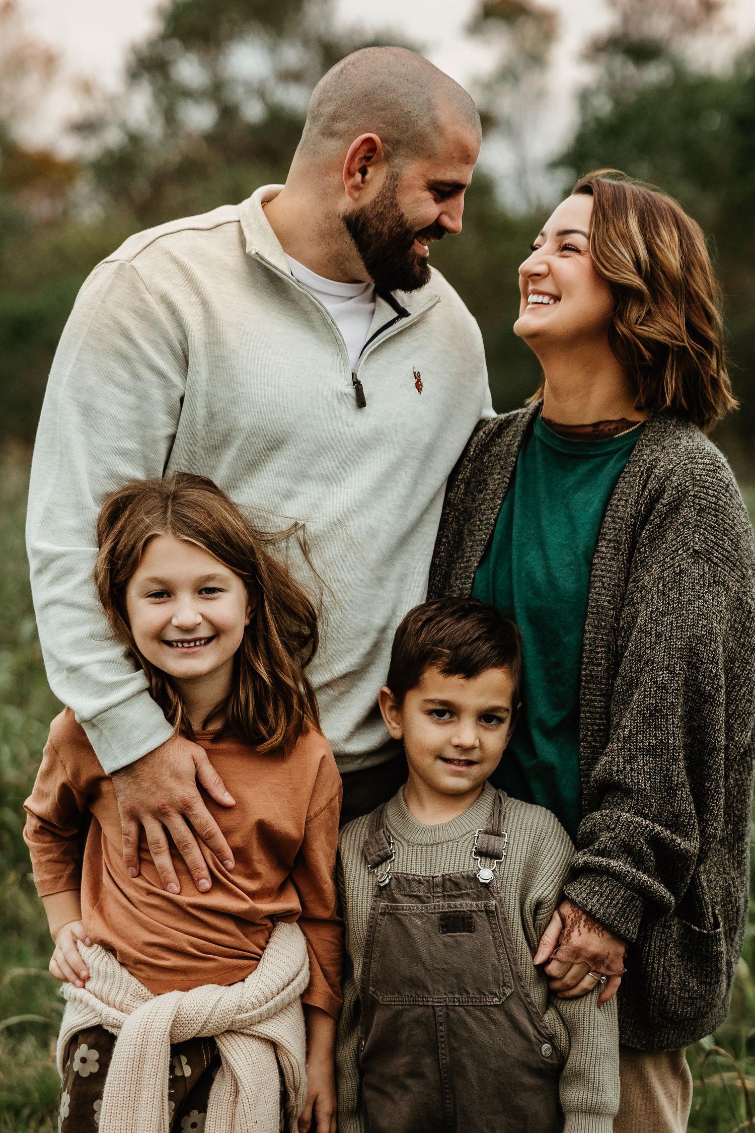 A loving family of four shares a joyful candid moment together outdoors wearing casual fall clothing.