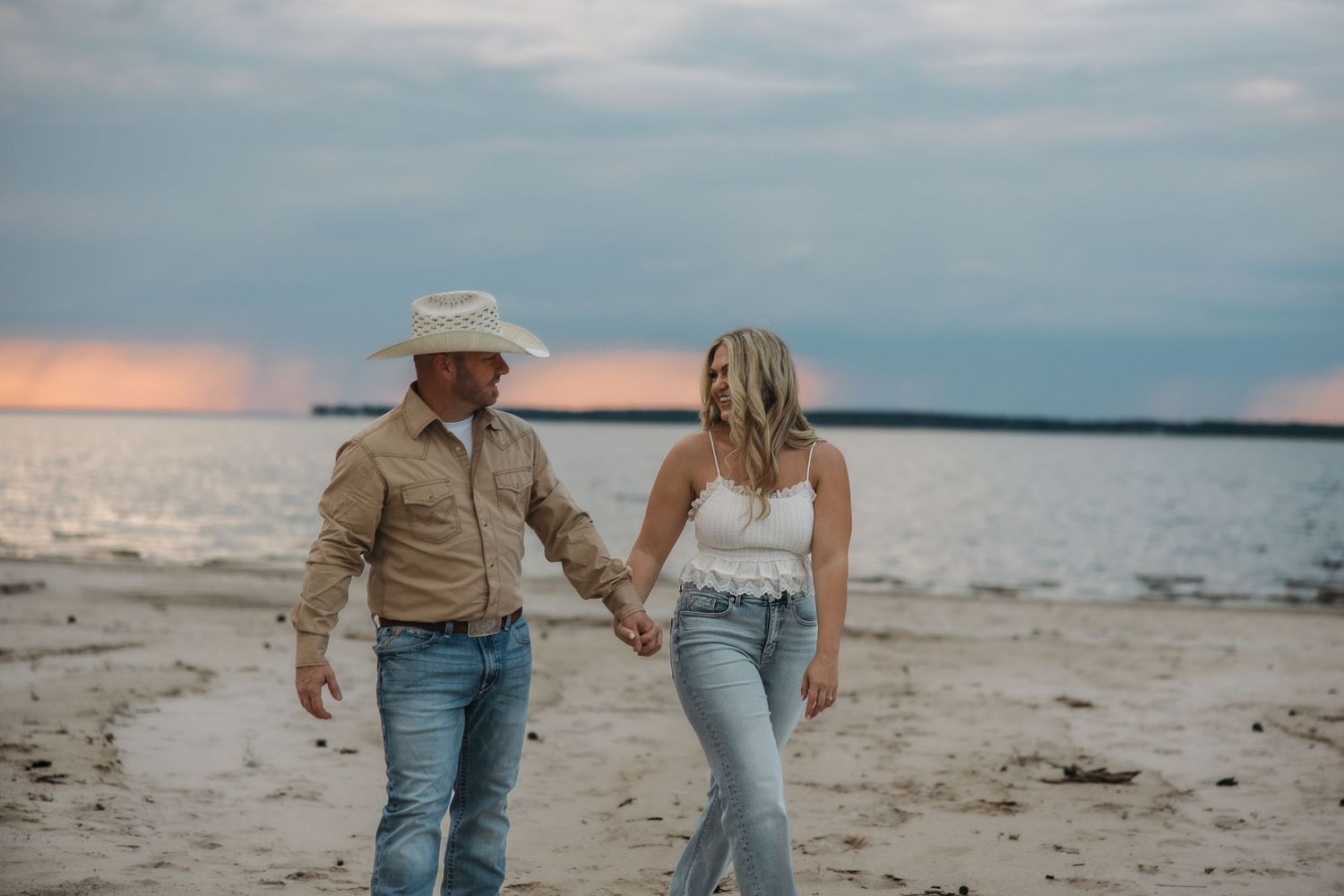 Two people stroll together on a peaceful beach shoreline during golden hour with moody clouds above.