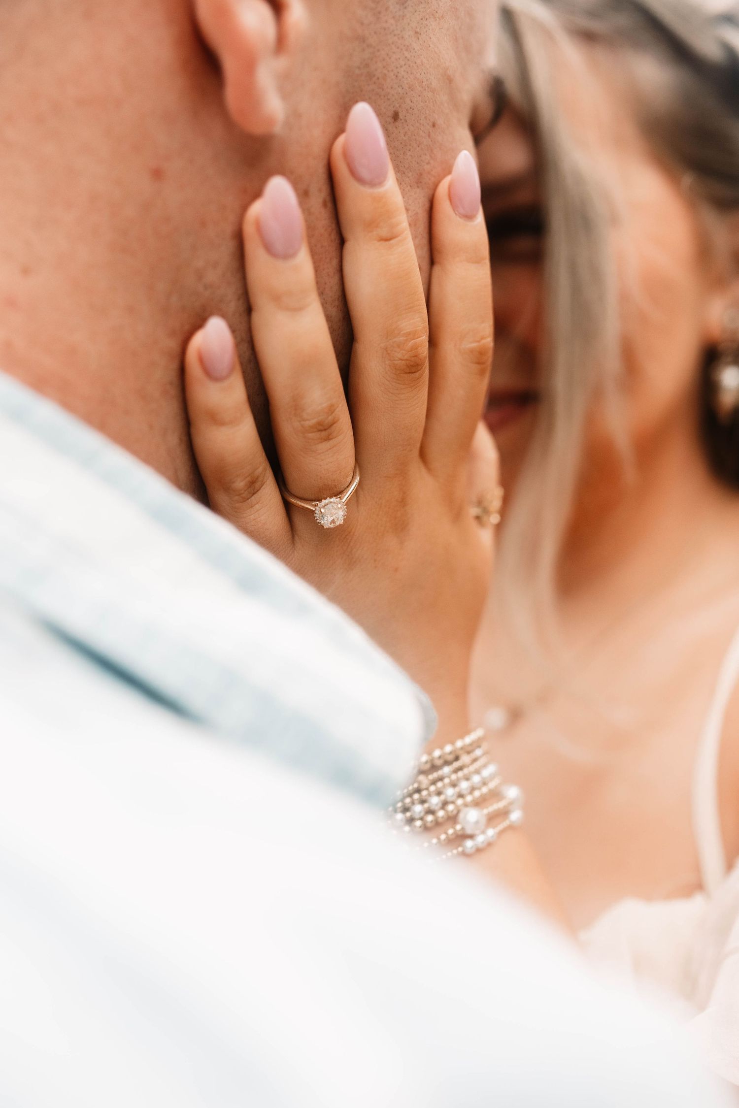 Close-up of manicured hands with engagement ring and pearl bracelet during romantic wedding moment.