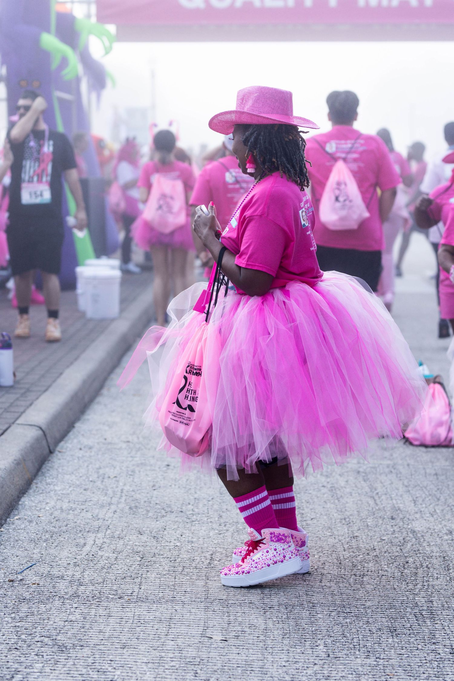 Participant in bright pink tutu and hat at charity race wearing matching pink t-shirt and athletic shoes.