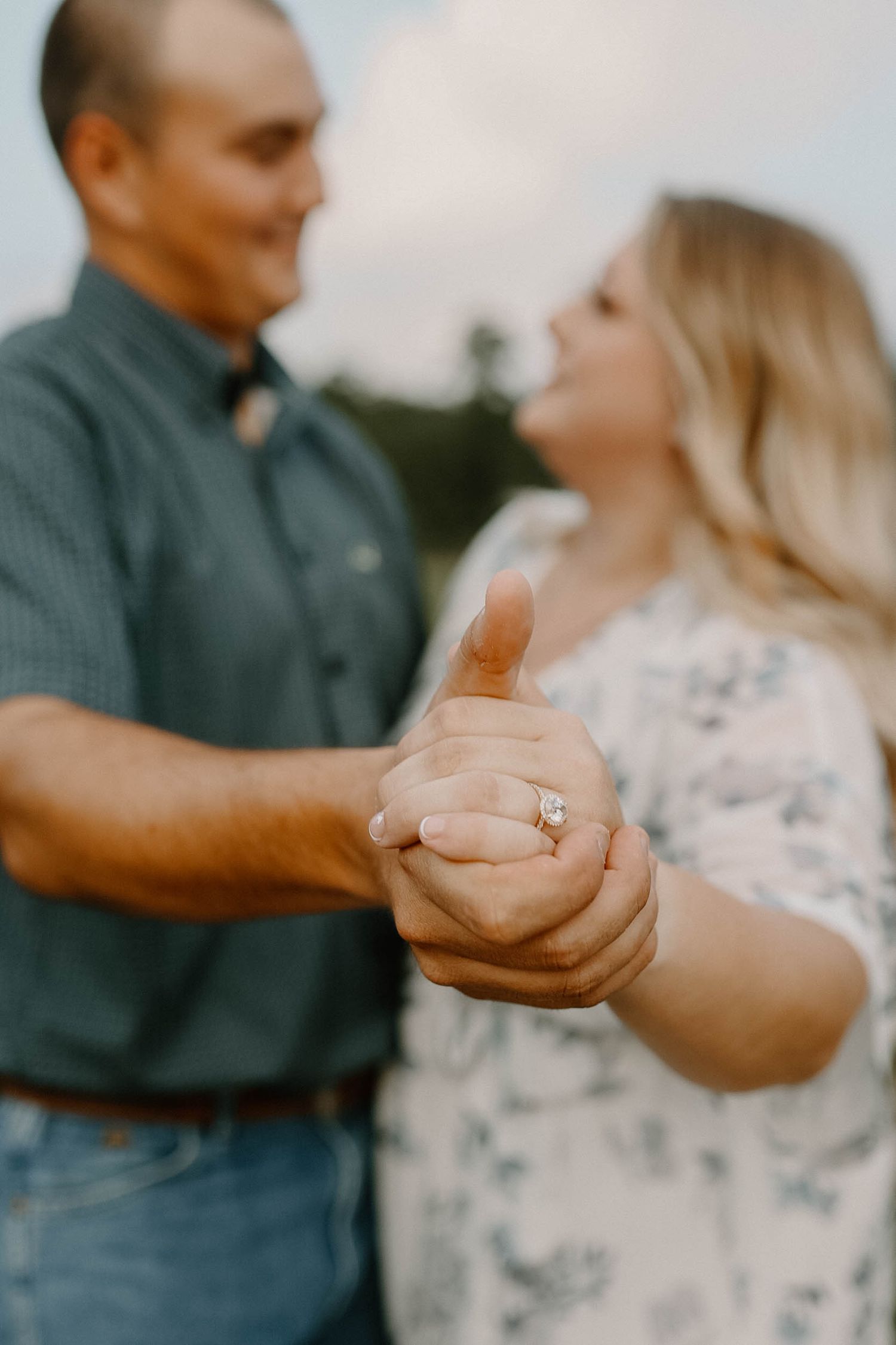 Close-up shot showing clasped hands with an engagement ring during a romantic outdoor photoshoot.