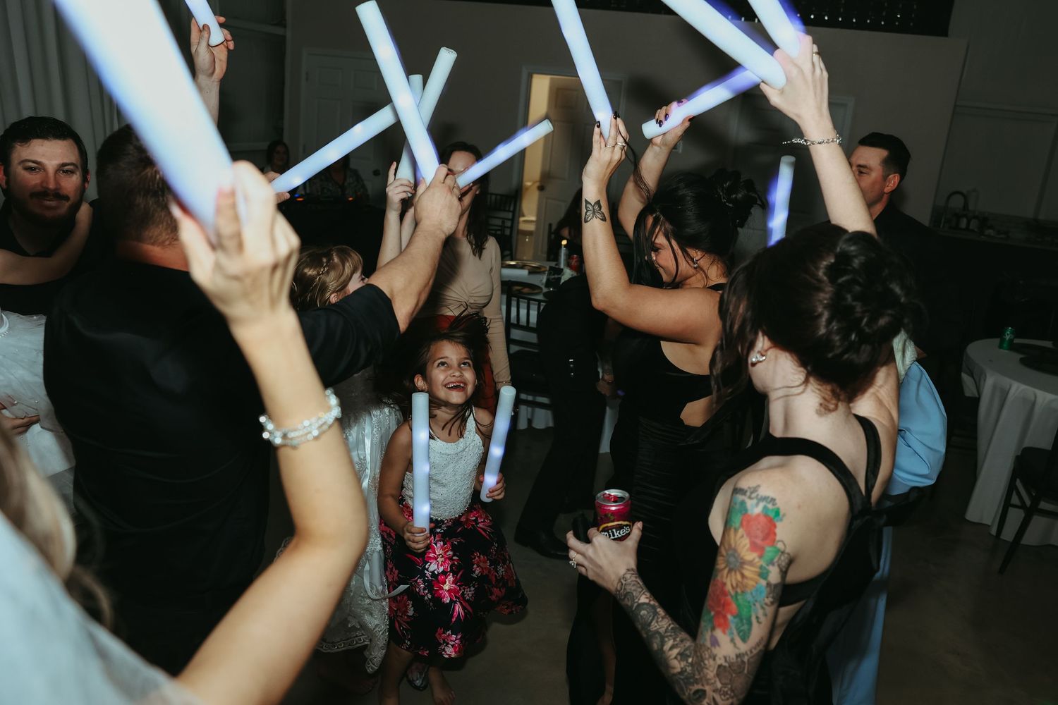 People dance with glowing blue light sticks at a dark indoor party.
