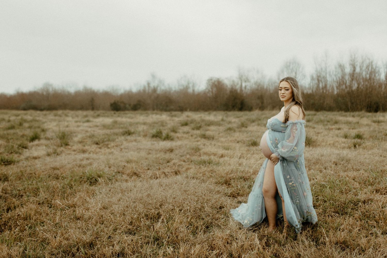 Figure in a flowing powder blue dress stands thoughtfully in a misty autumn field.