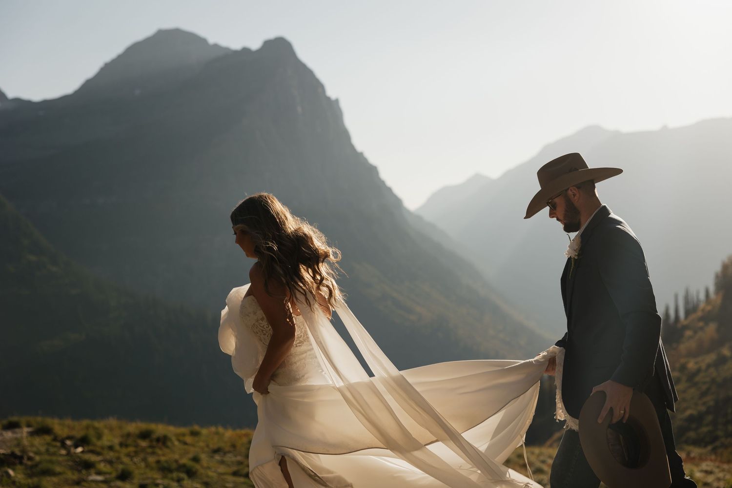 Couple in western attire share an intimate dance with mountains and sunlight in the background.