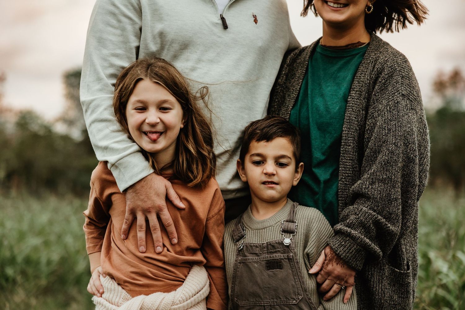Casually dressed family stands together in a grassy field during sunset in autumn.